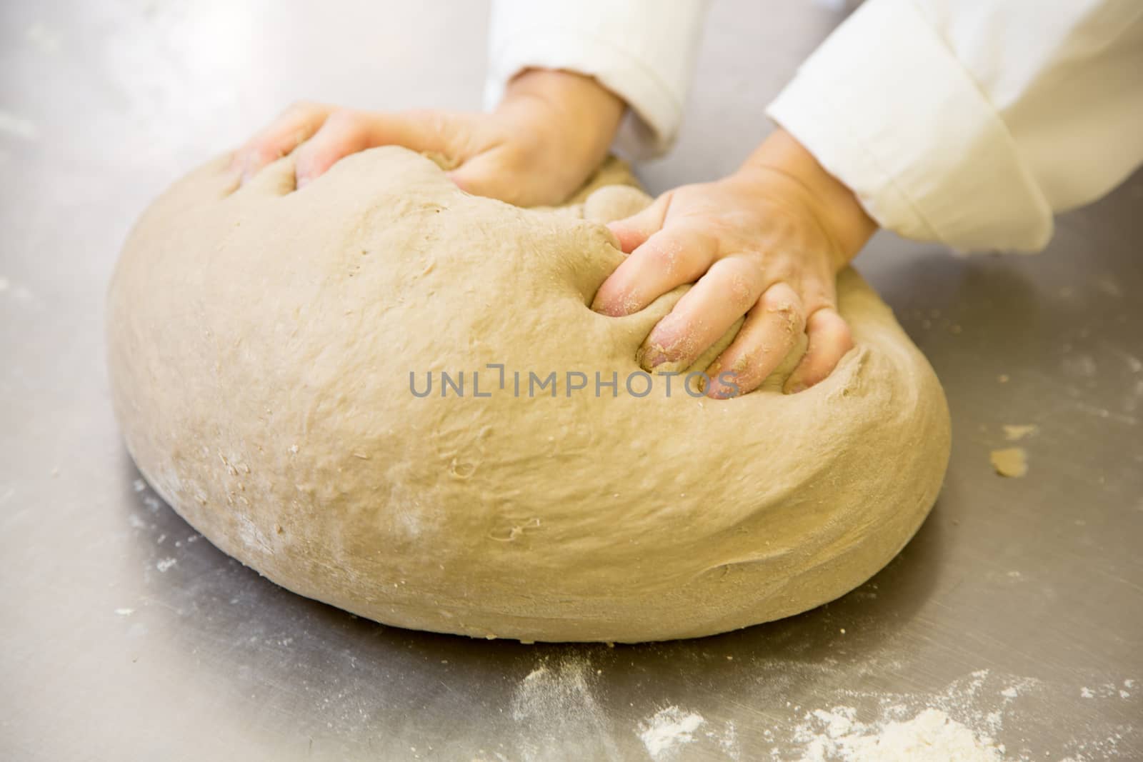Baker kneading bread dough in bakery or bakehouse