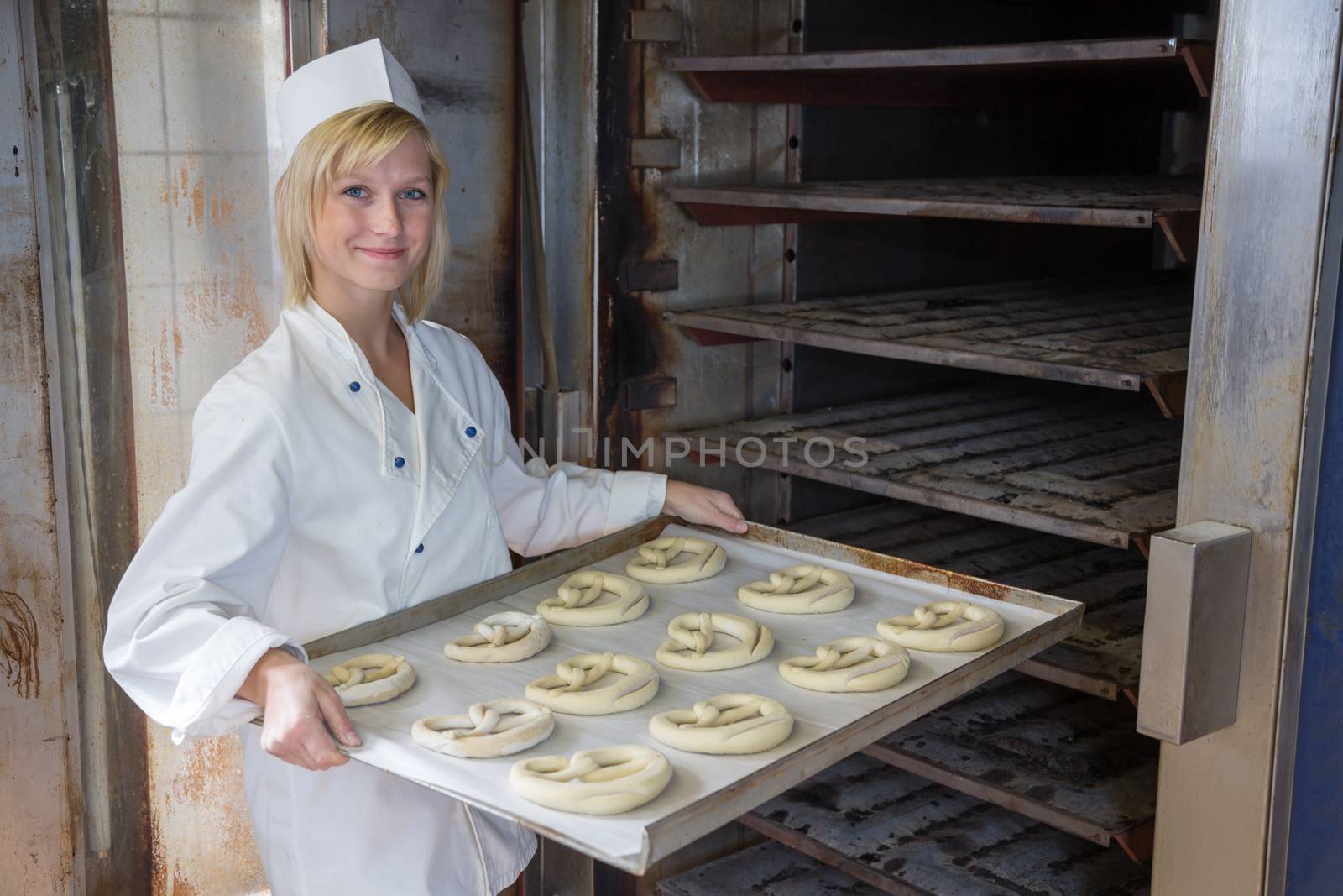 Baker putting pretzels into oven in a bakery by ikonoklast_fotografie