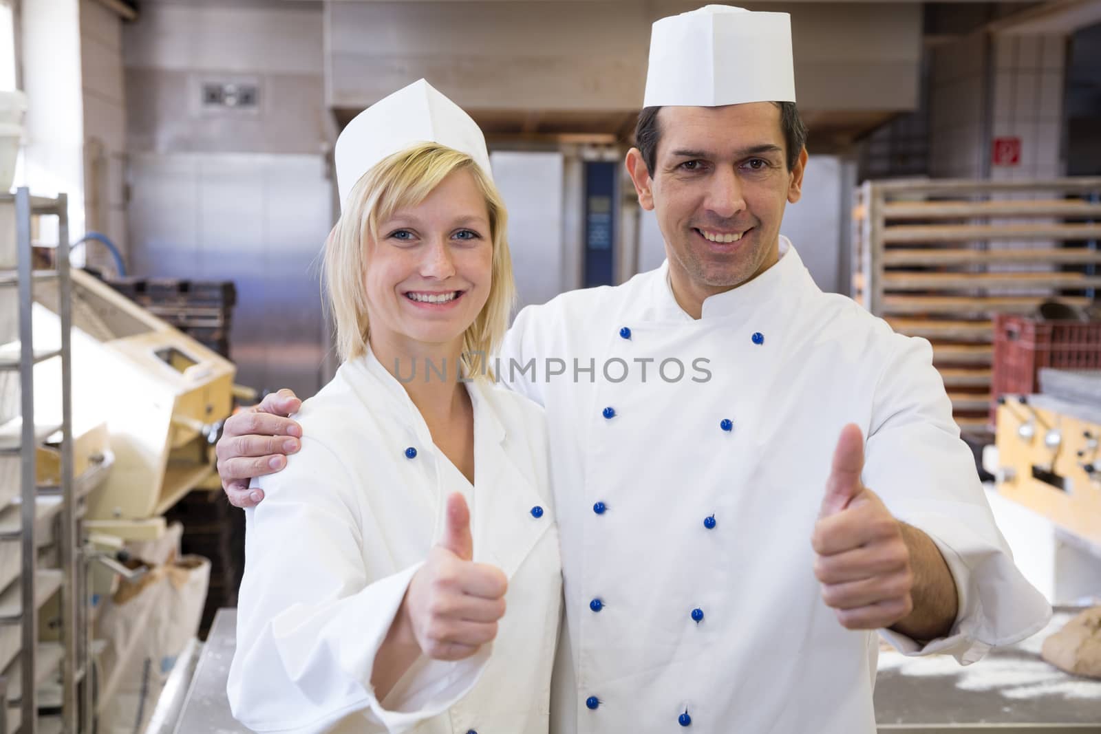 Two bakers showing thumbs up in bakery