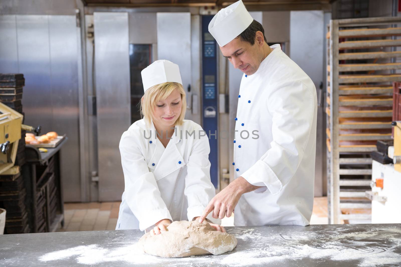 Baker instruction apprentice in kneading bread dough by ikonoklast_fotografie