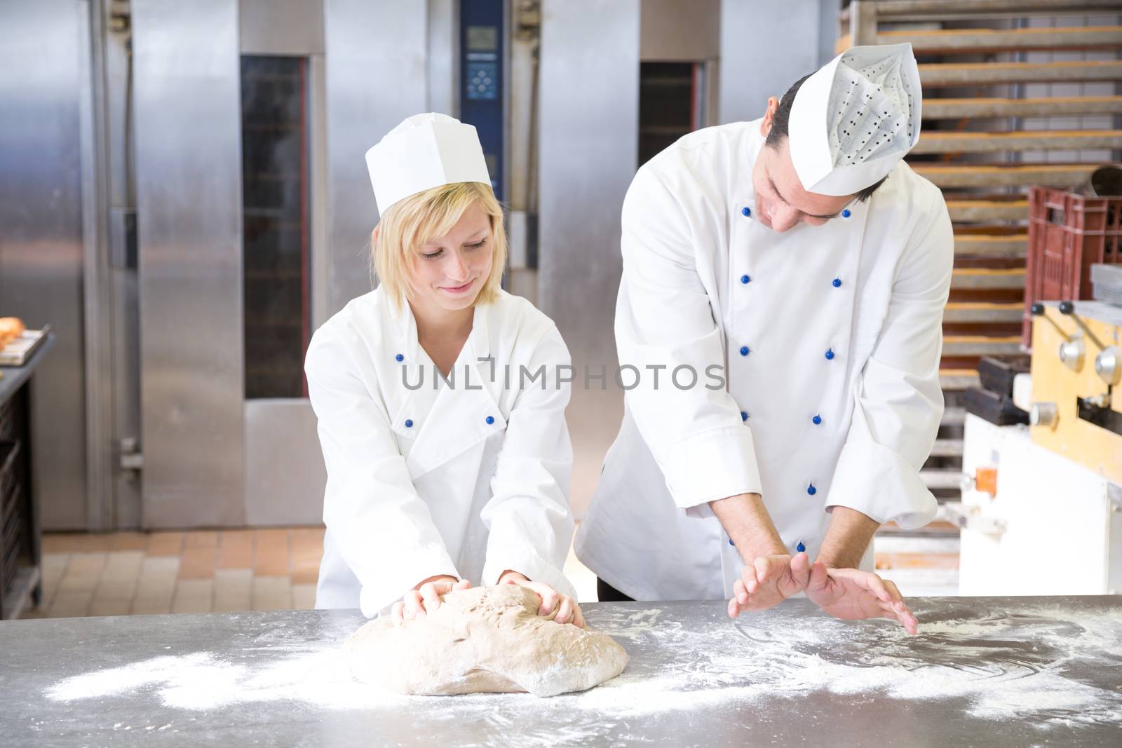 Baker instructing apprentice how to knead dough properly