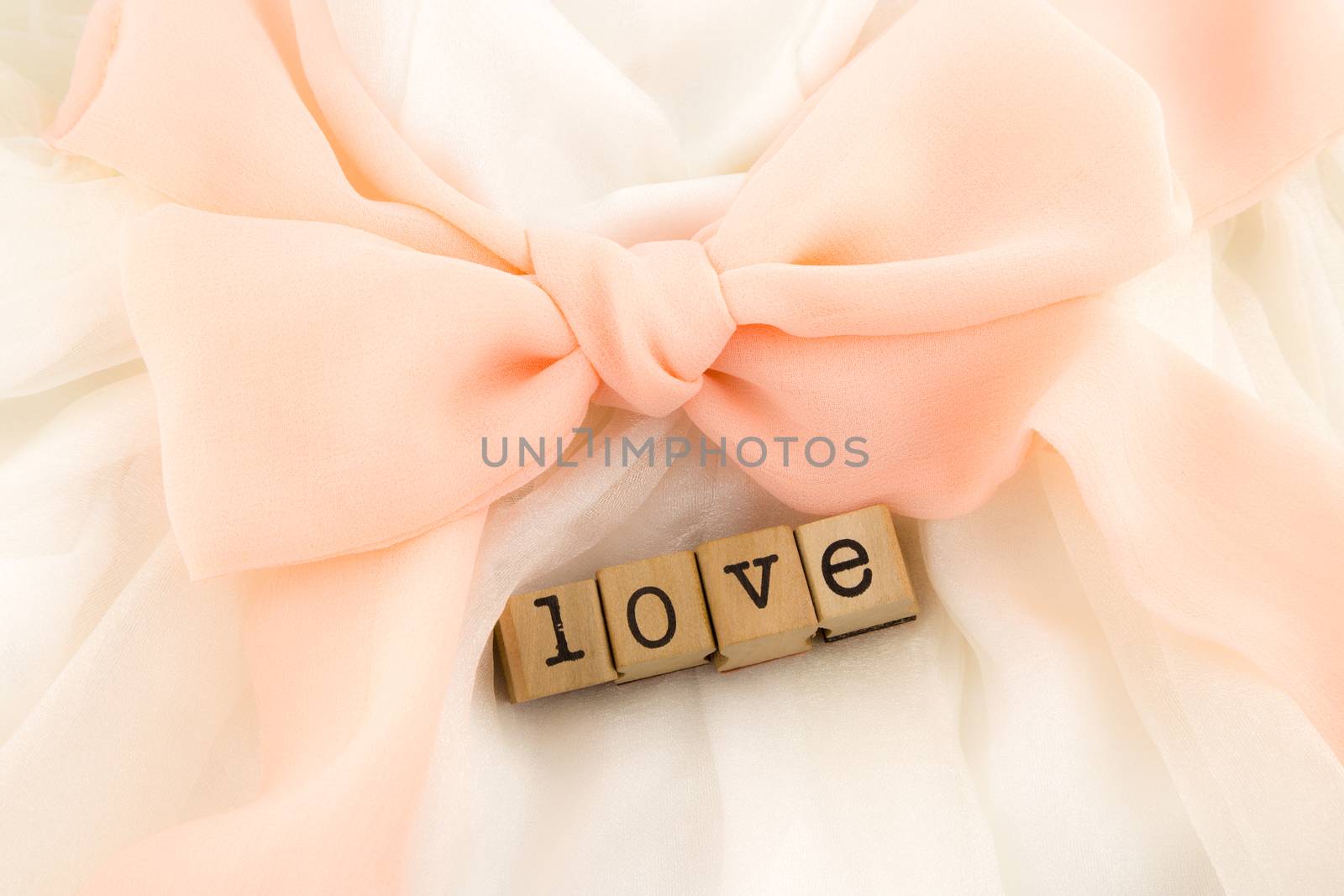 closeup love wording and dress with peach bow ribbon, white soft textiles, wedding concept and idea