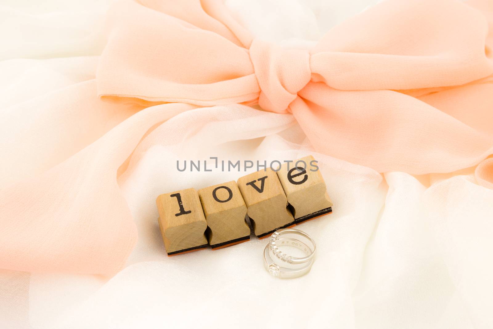 closeup love wording and rings on dress with peach bow ribbon, white soft textiles, wedding concept and idea
