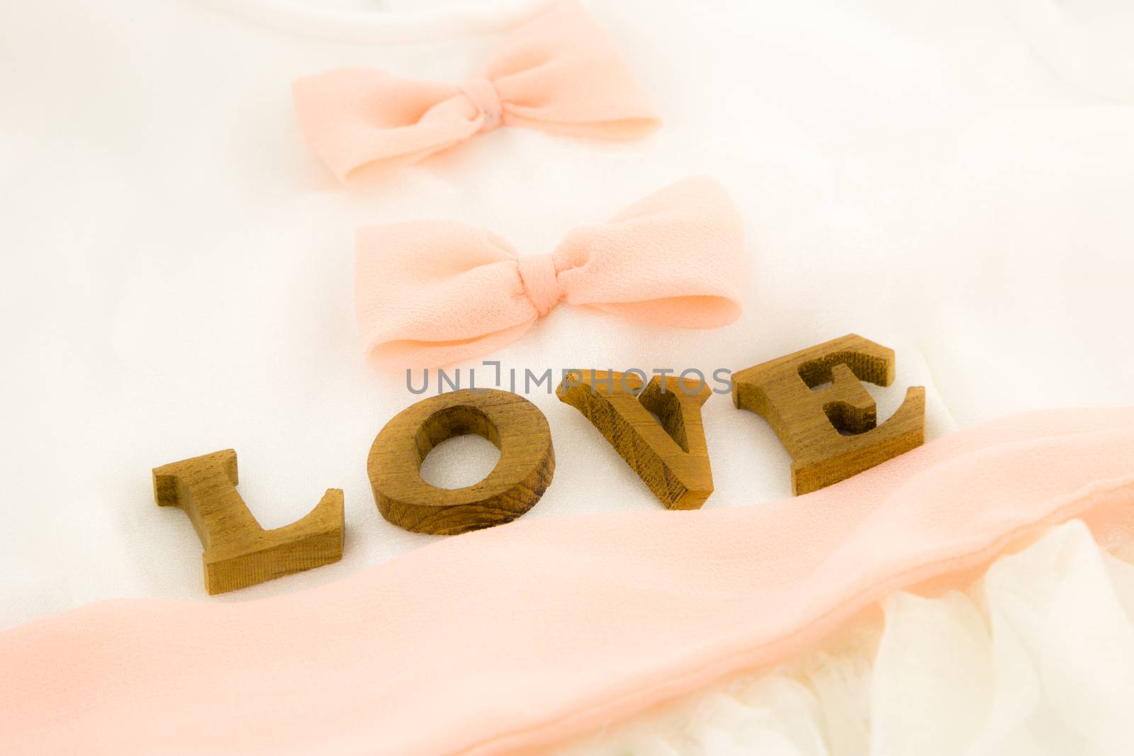 closeup love wording and dress with peach bow ribbon, white soft textiles, wedding concept and idea