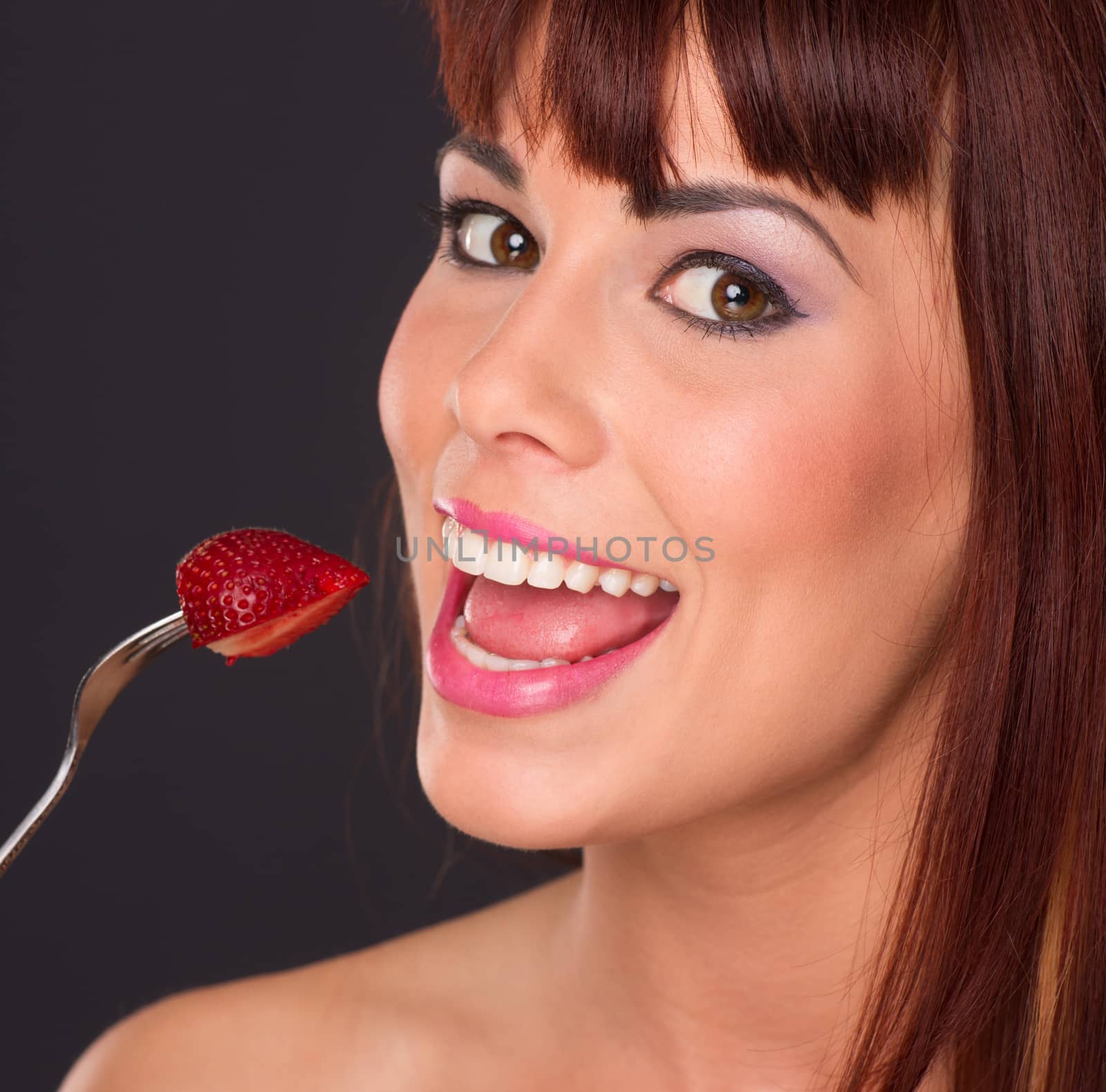Bright beautiful woman holds a fork loaded with fresh fruit strawberry