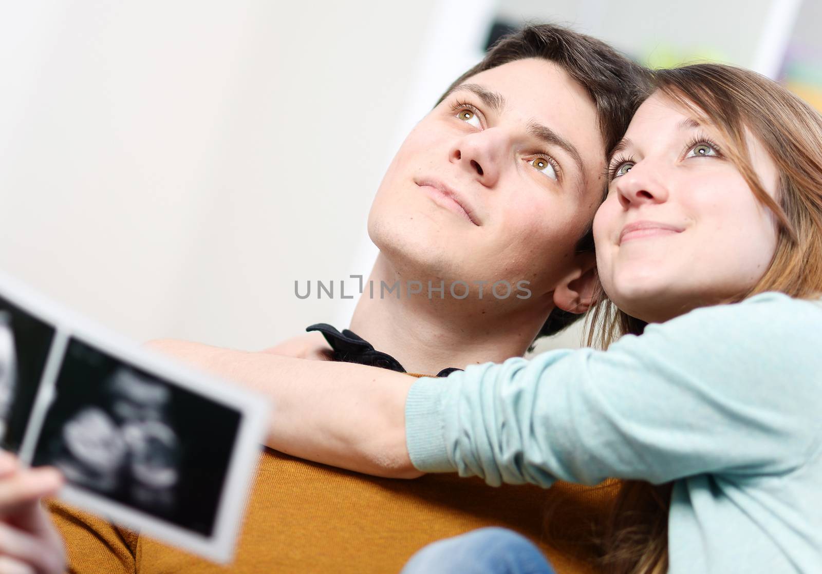 Beautiful couple imagines the future of their unborn child with ultrasound pictures in hands