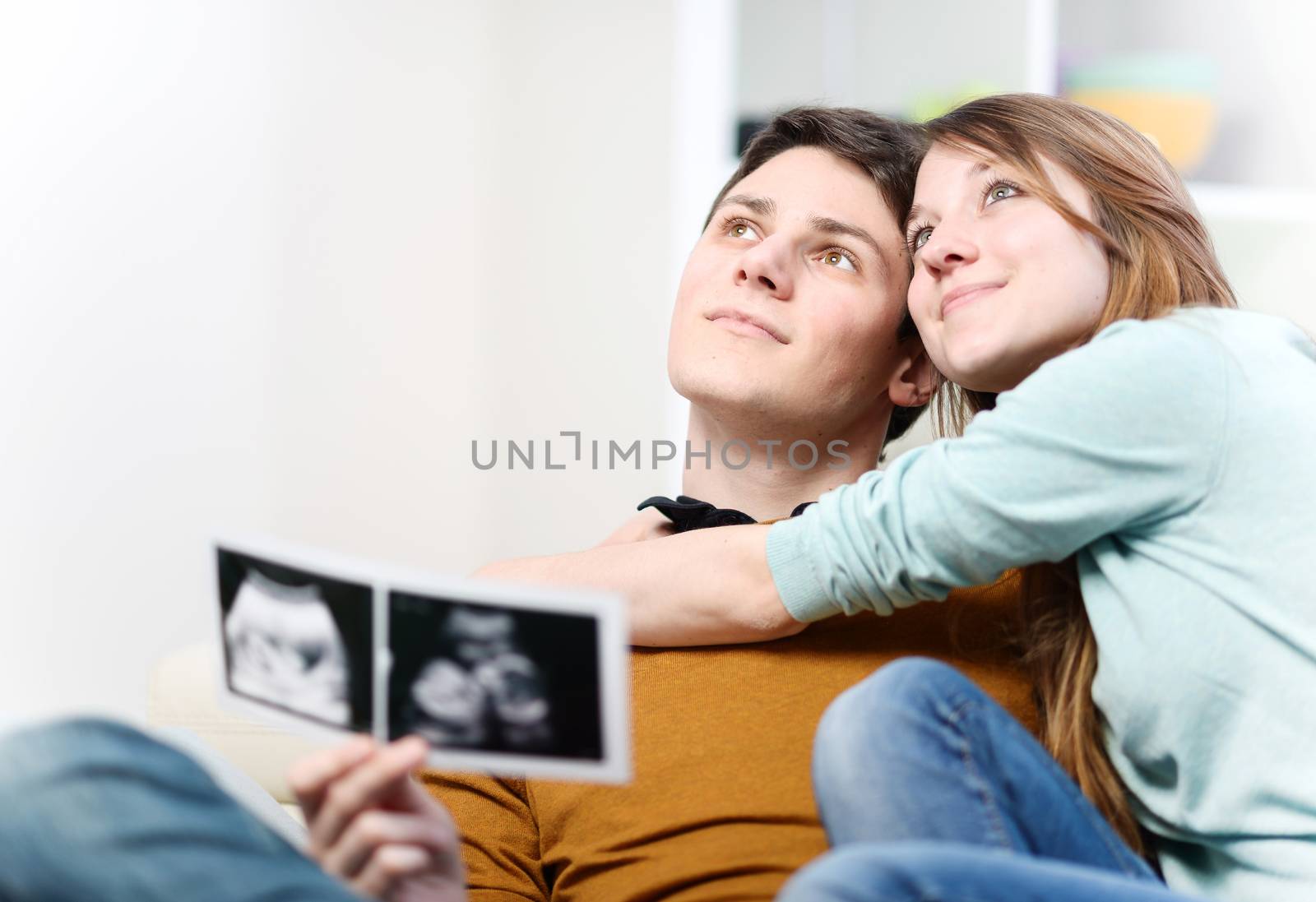 Beautiful couple imagines the future of their unborn child with ultrasound pictures in hands