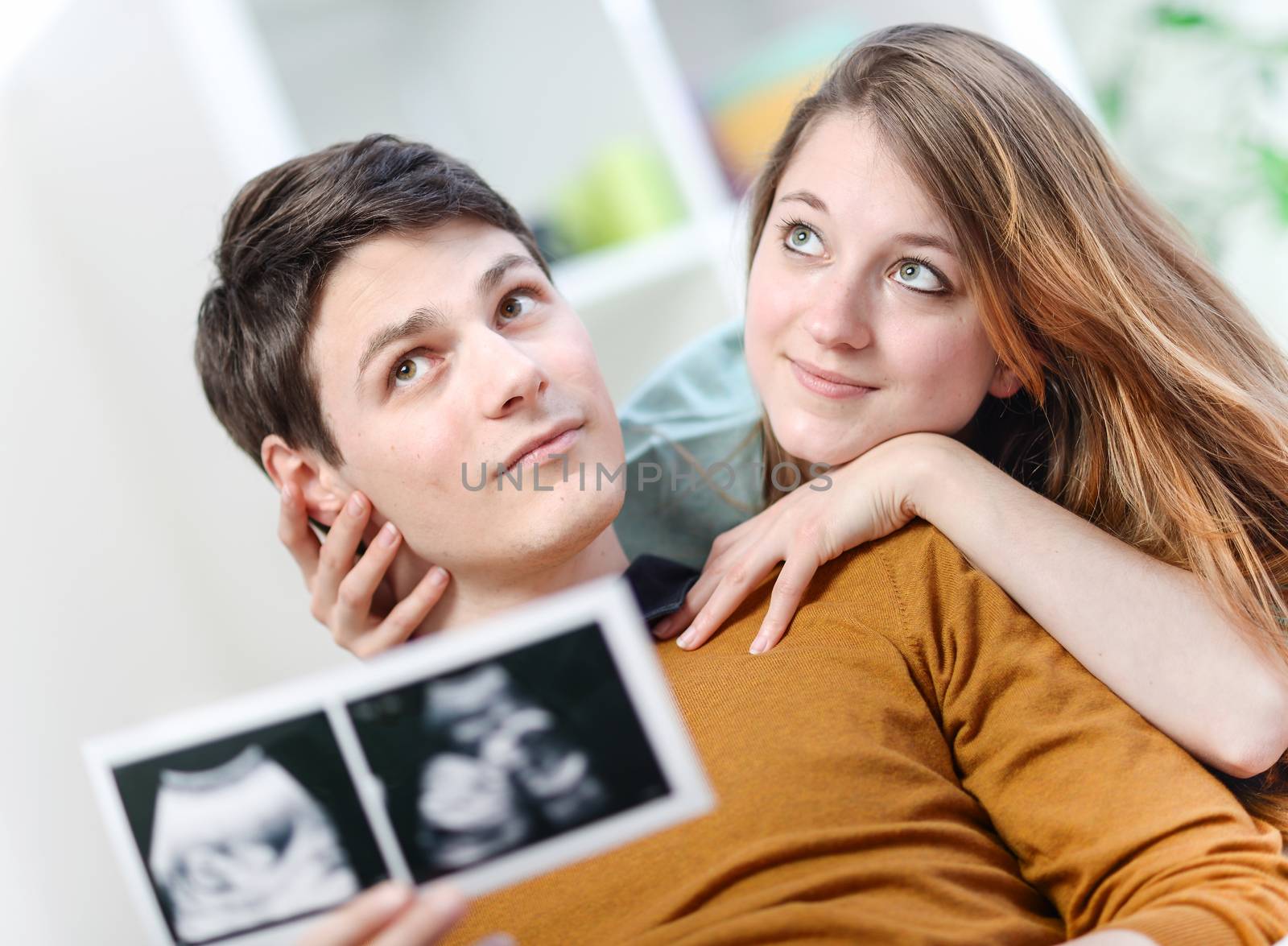 Beautiful couple imagines the future of their unborn child with ultrasound pictures in hands