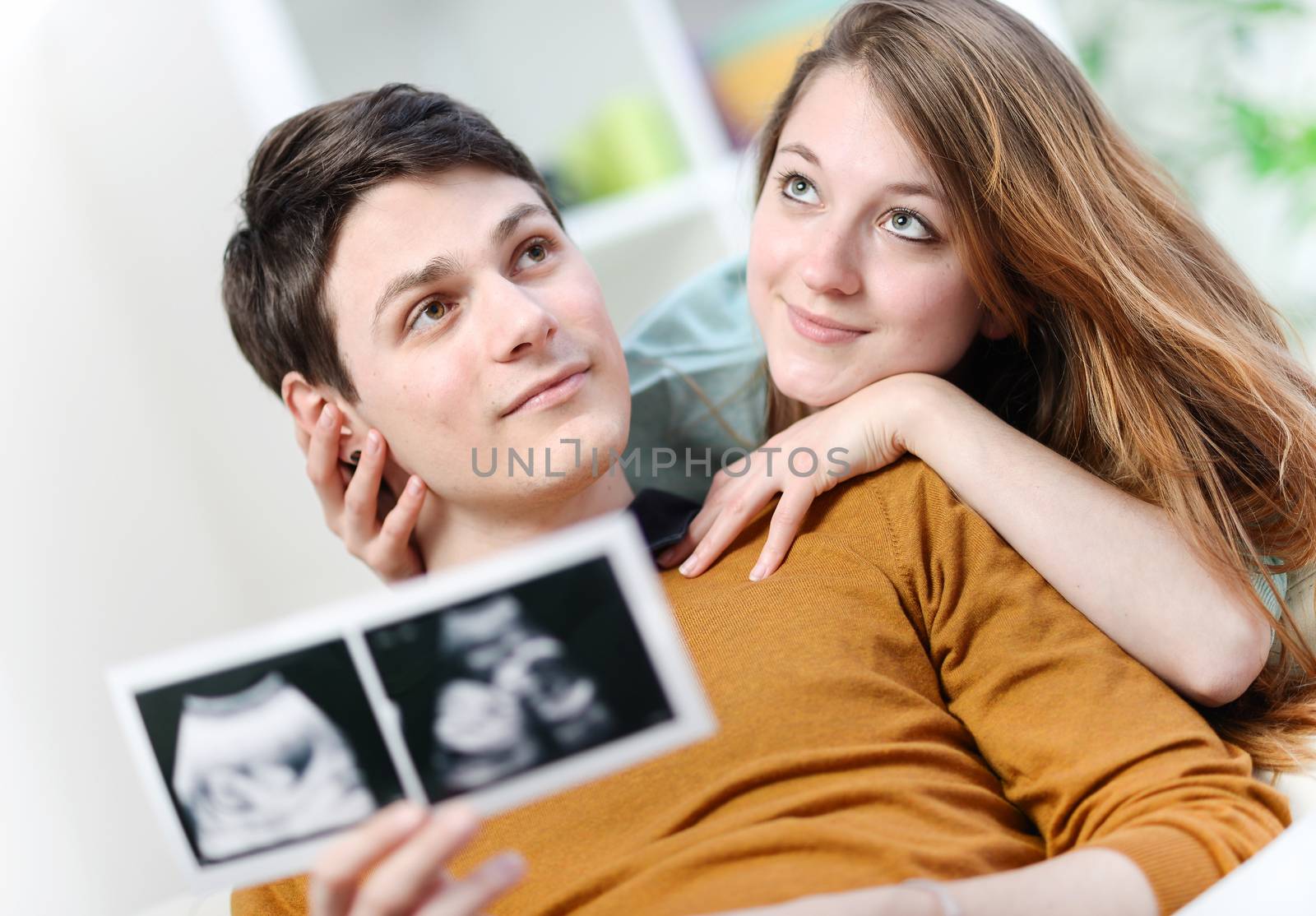 Cute couple imagines the future of their unborn child with ultrasound pictures in hands