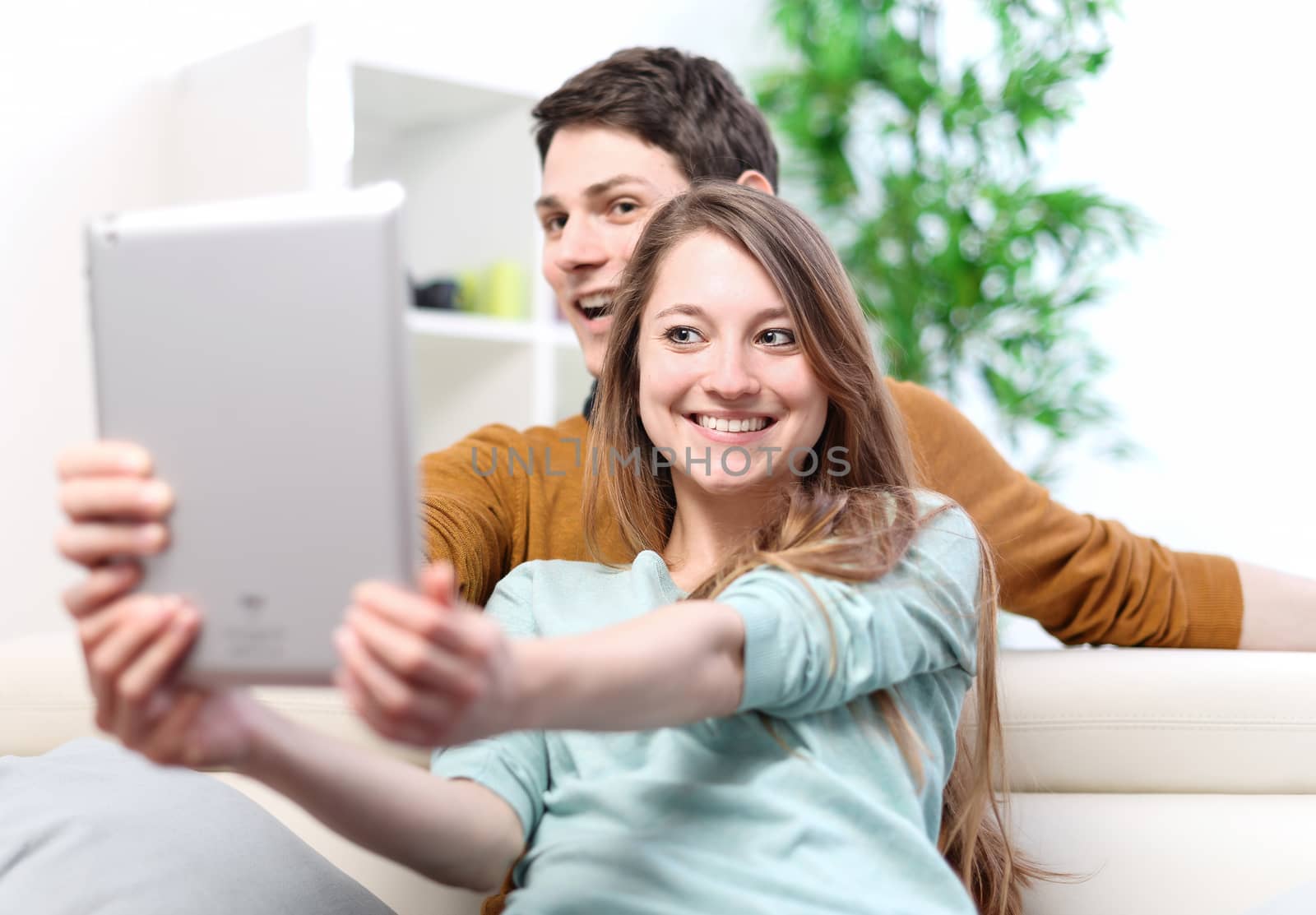 Two happy friends taking photo with tablet pc at home on the couch