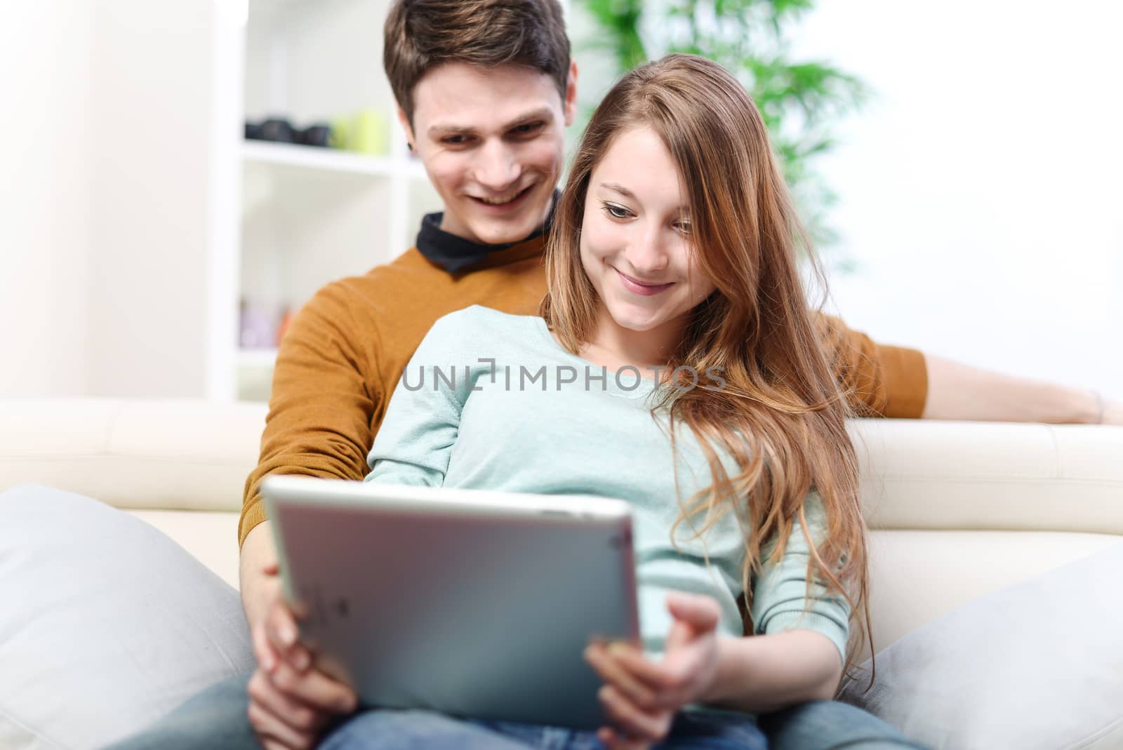 Young couple using digital tablet indoors on the sofa by pixinoo