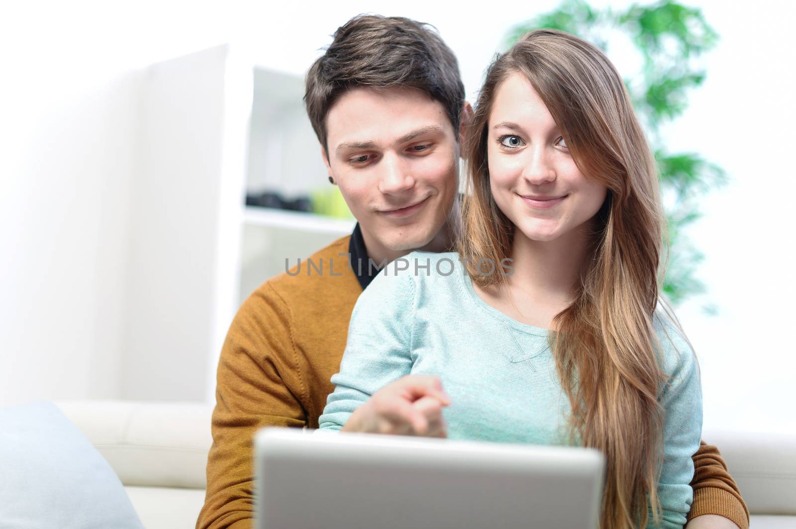 Portrait of a smiling young couple using laptop at home indoor by pixinoo