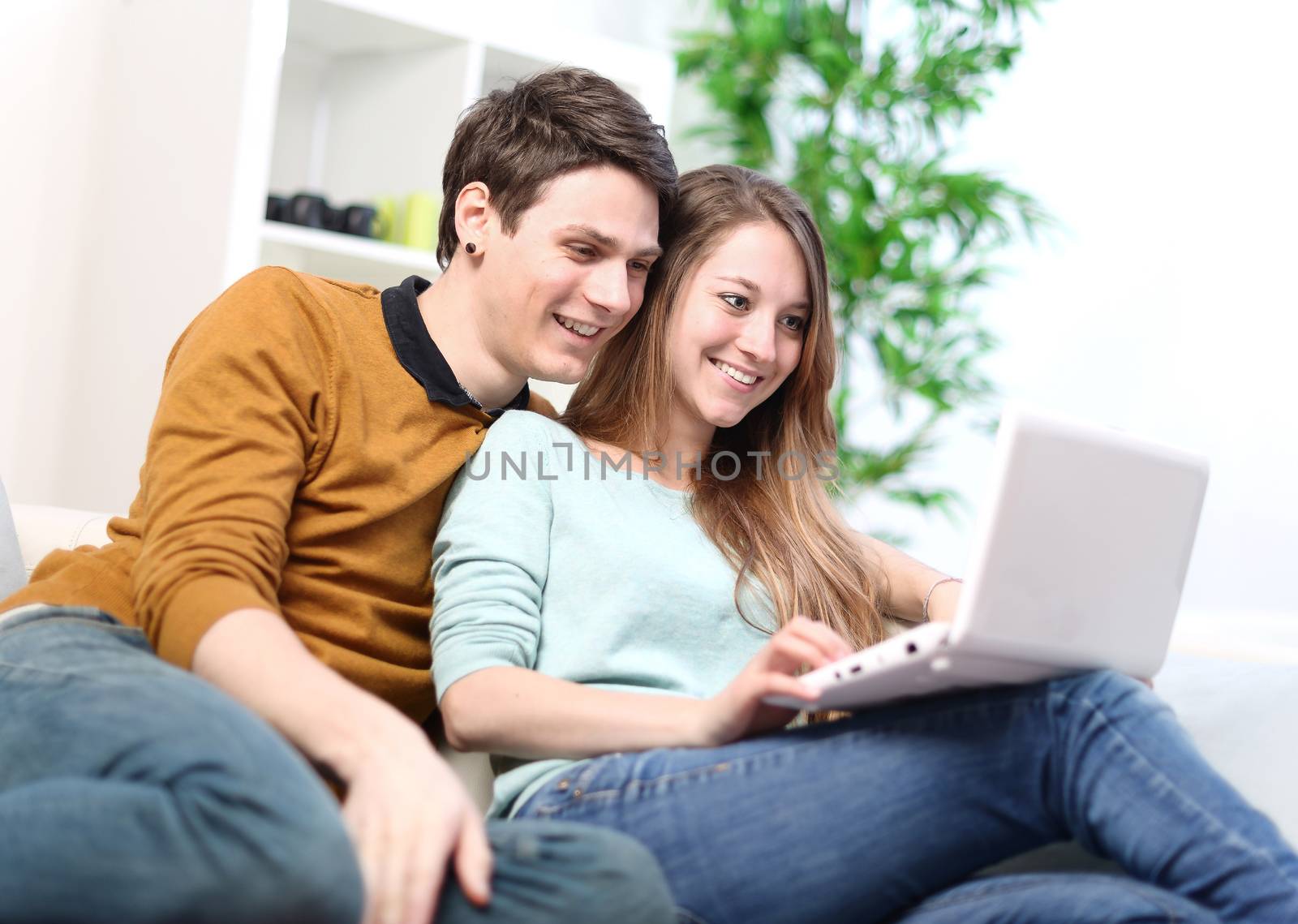 Portrait of a smiling young couple using laptop at home indoor by pixinoo