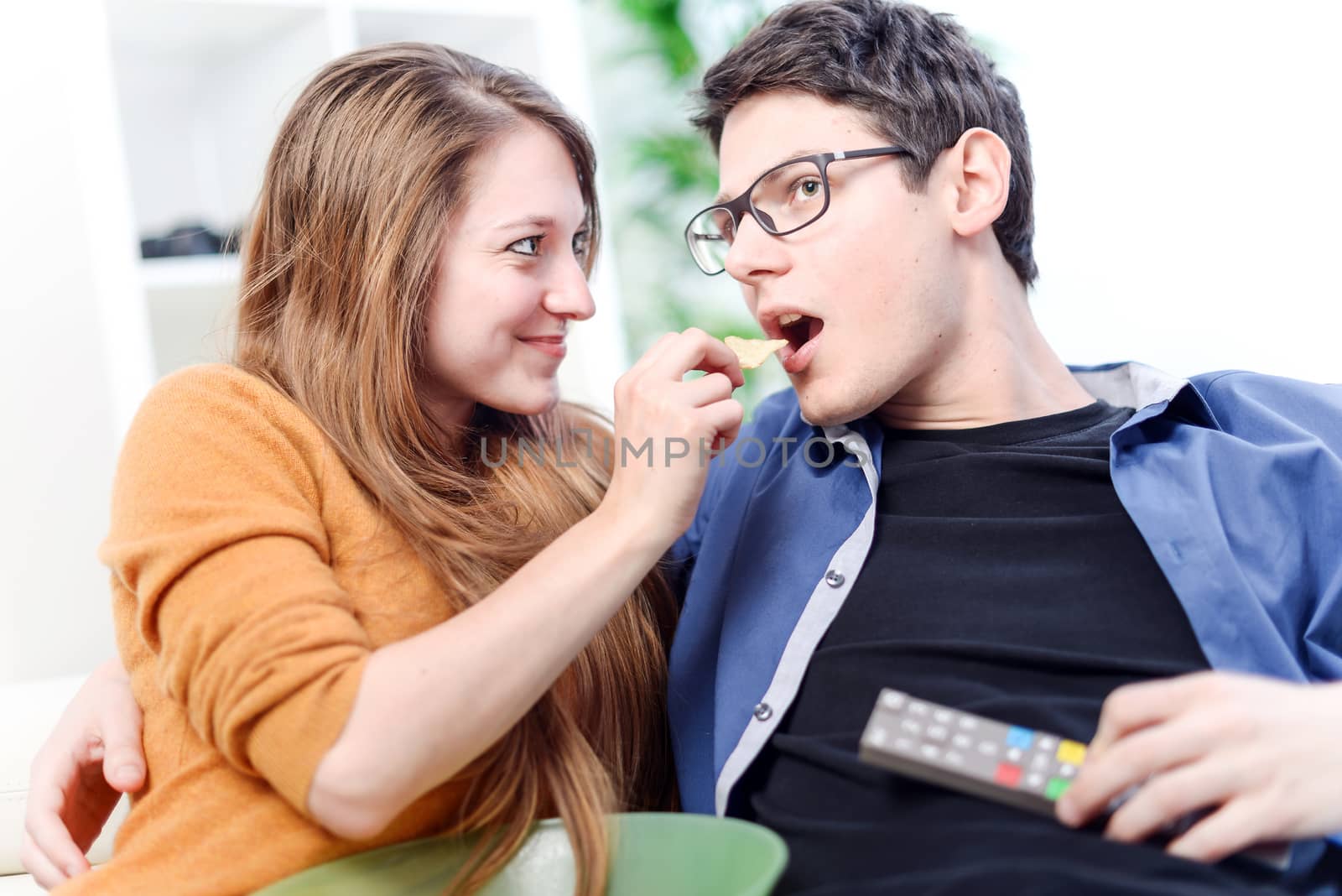 beautiful young woman giving food to her darling front of the TV