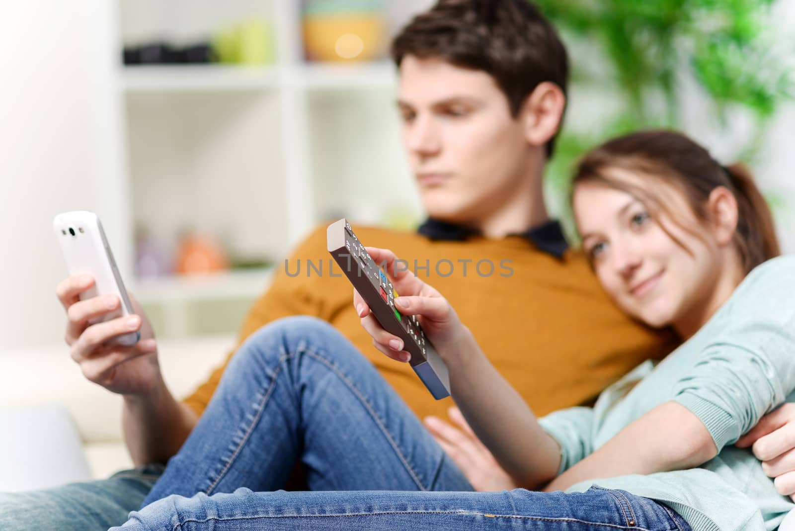 beautiful woman watching tv while her lover is watching a screen of cell