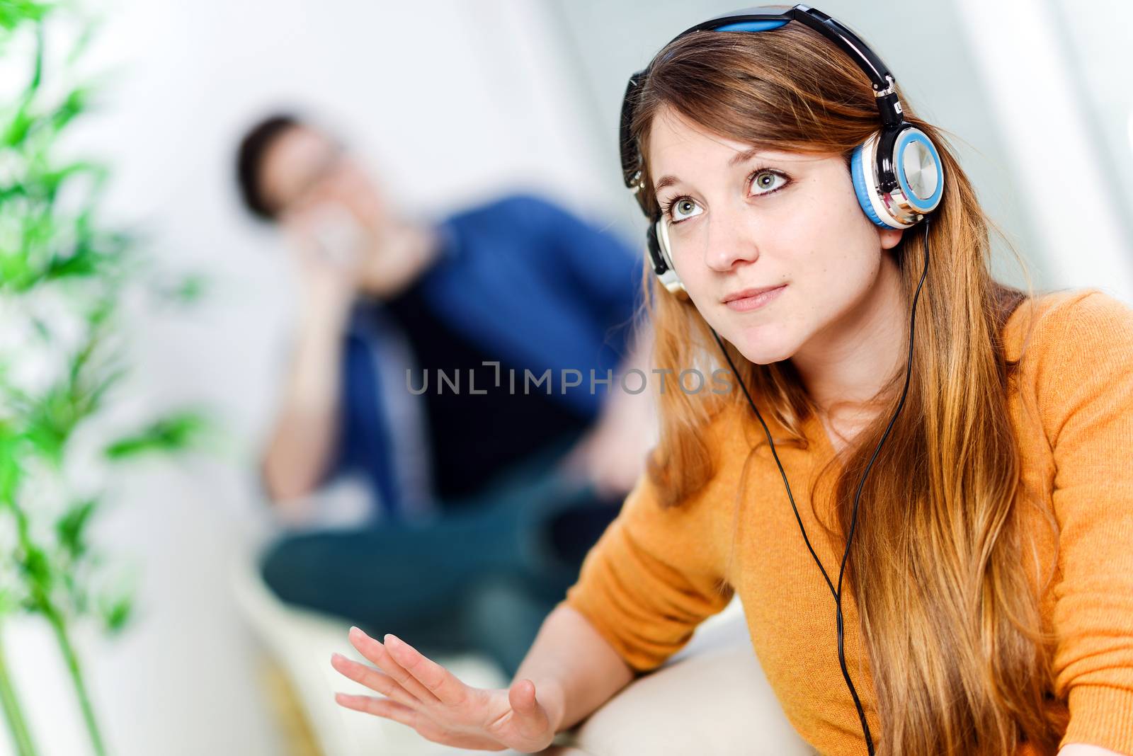 Beautiful blond listening to some music while her boyfriend is bored