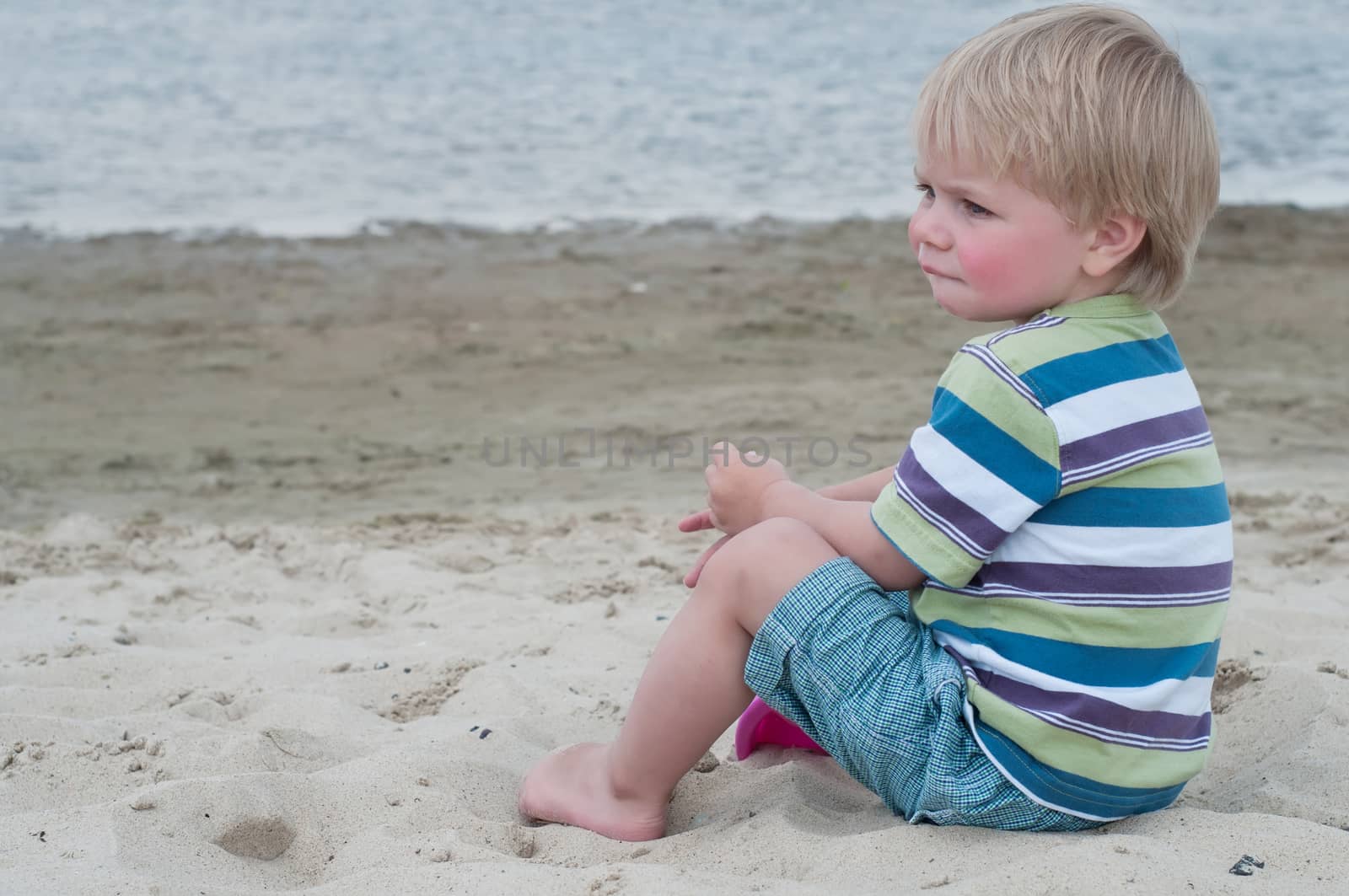 Little boy in striped t-hirt sitting on the beach