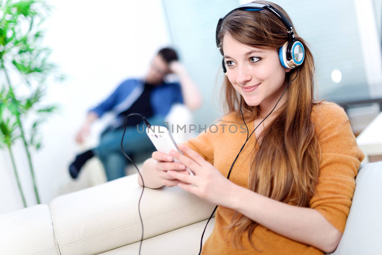 Beautiful blond listening to some music while her boyfriend is bored