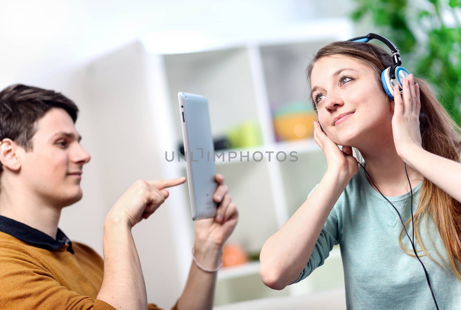 Pretty woman listening to music with her headphones while her husband takes pictures with a tablet