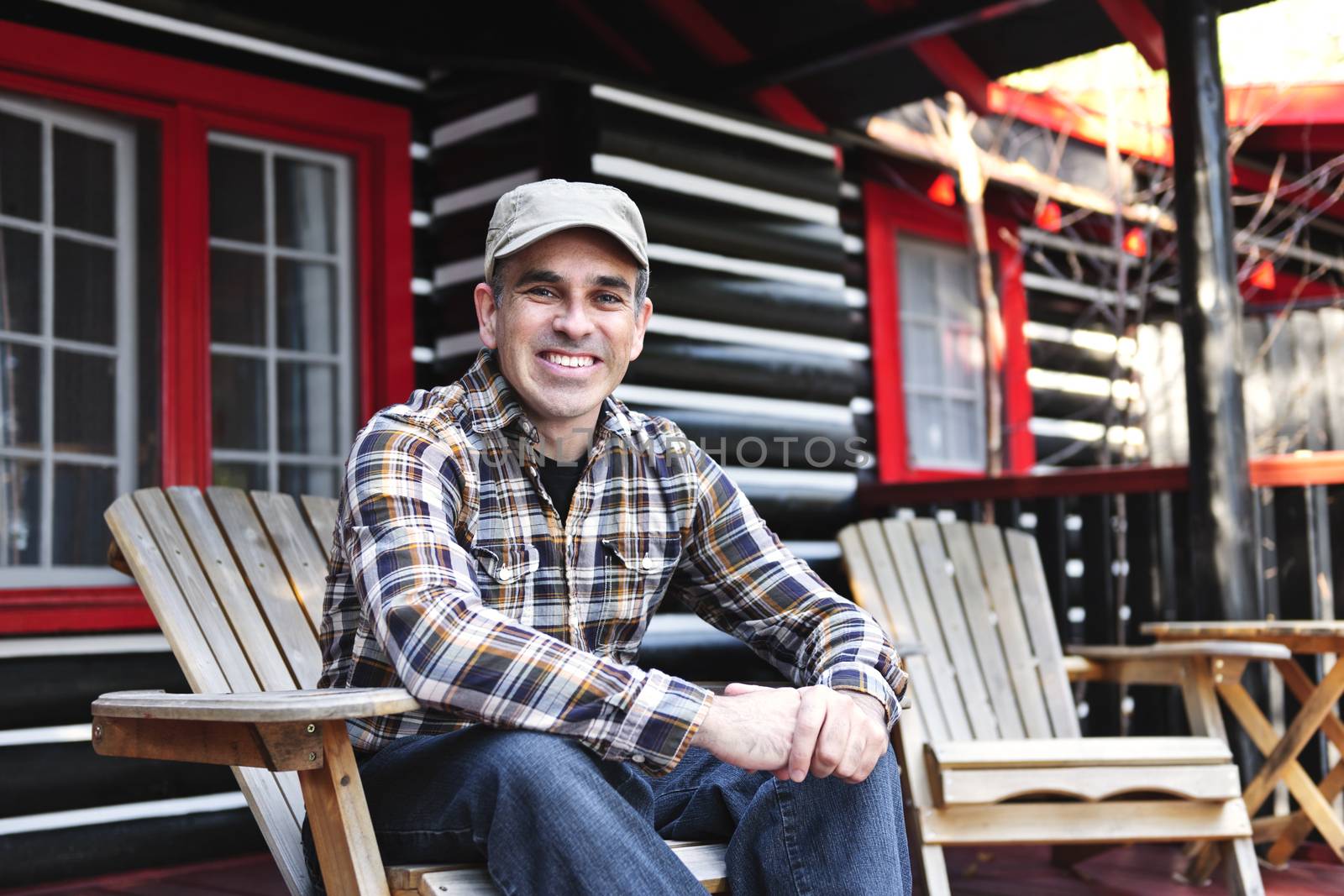 Smiling man sitting on cottage deck in wooden adirondack chair