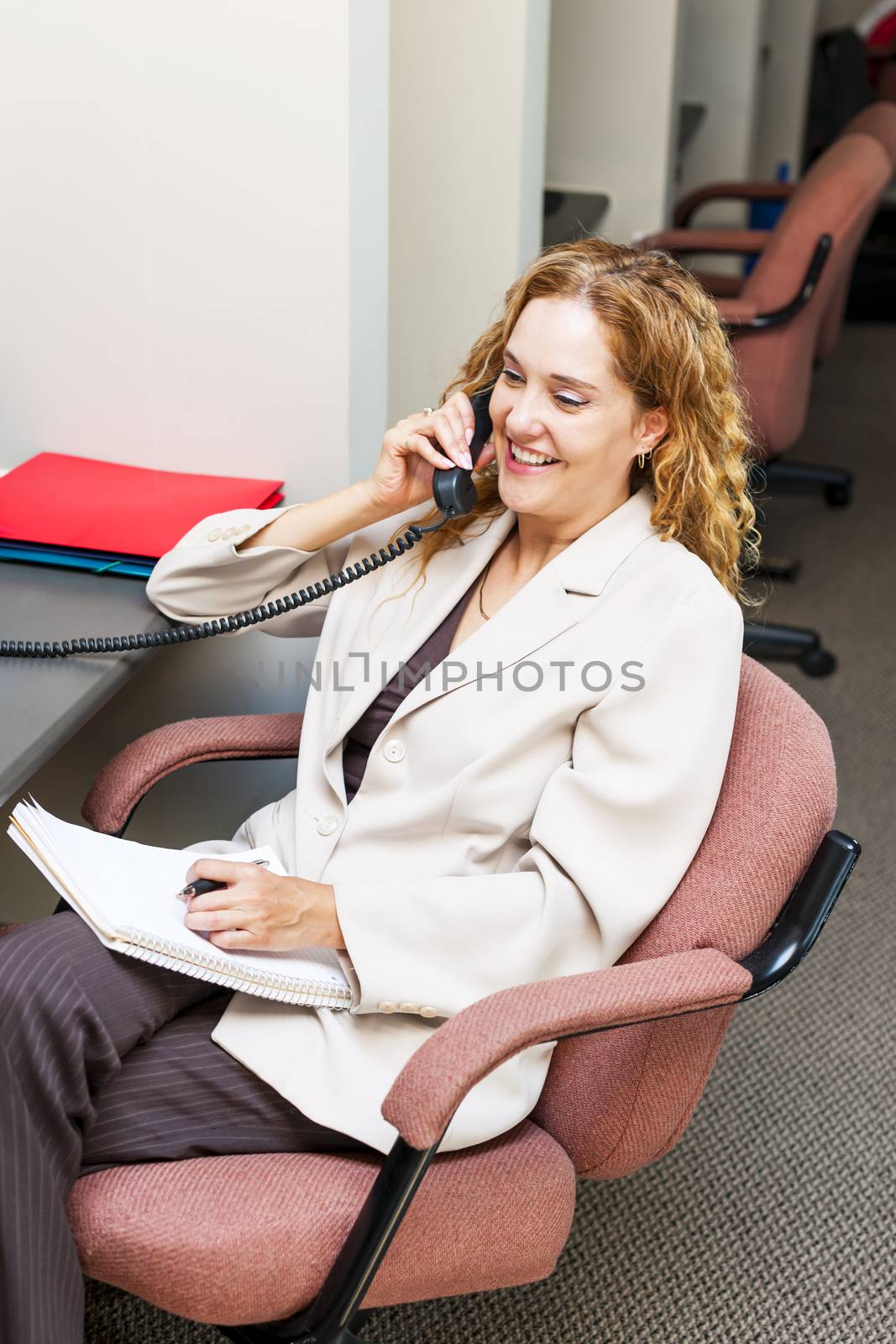 Happy businesswoman on phone taking notes in office workstation