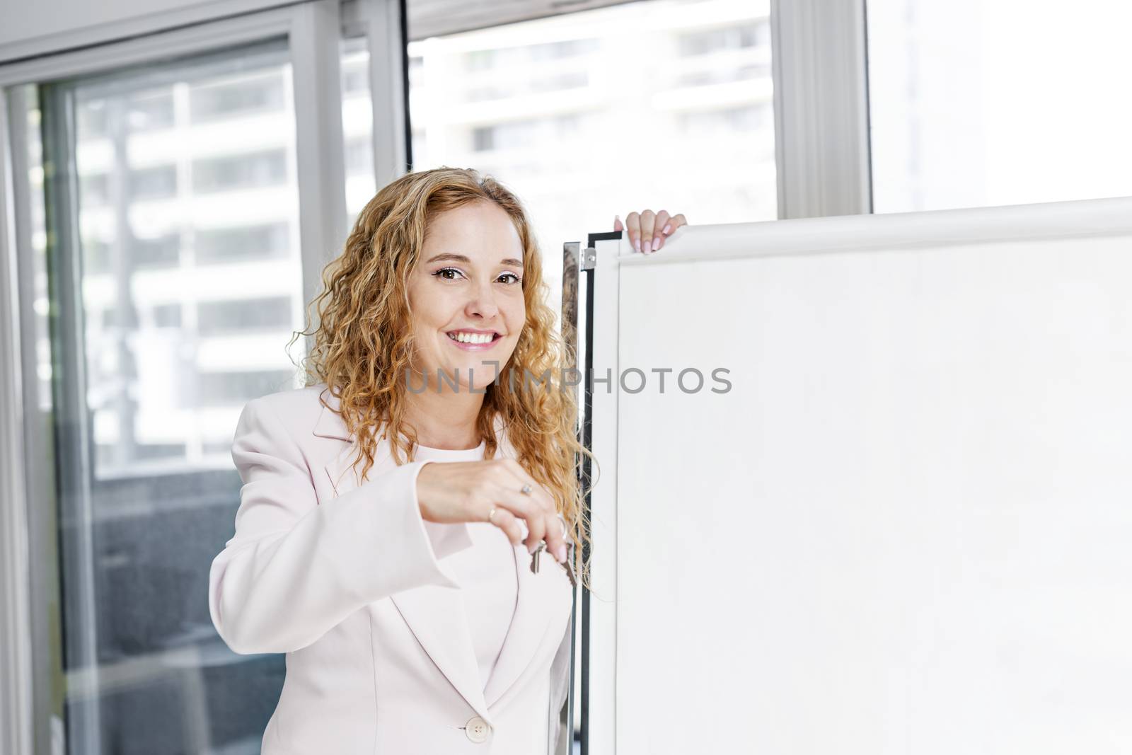 Smiling female real estate agent offering keys standing with blank flip chart