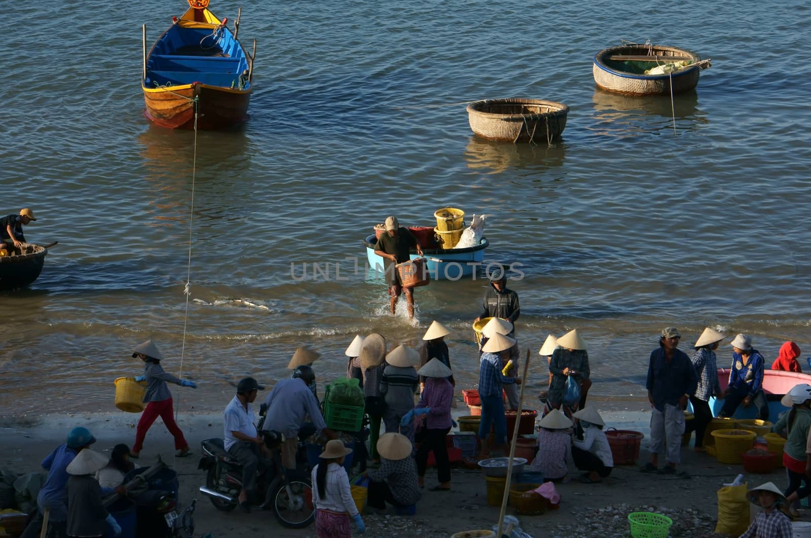 PHAN THIET, VIET NAM- FEB 3: Crowded scene of people buy and sale seafood at market on baach, man carry fish from boat, woman choose and bargain to buy fishes in Phan Thiet, Viet Nam on Feb 3, 2013