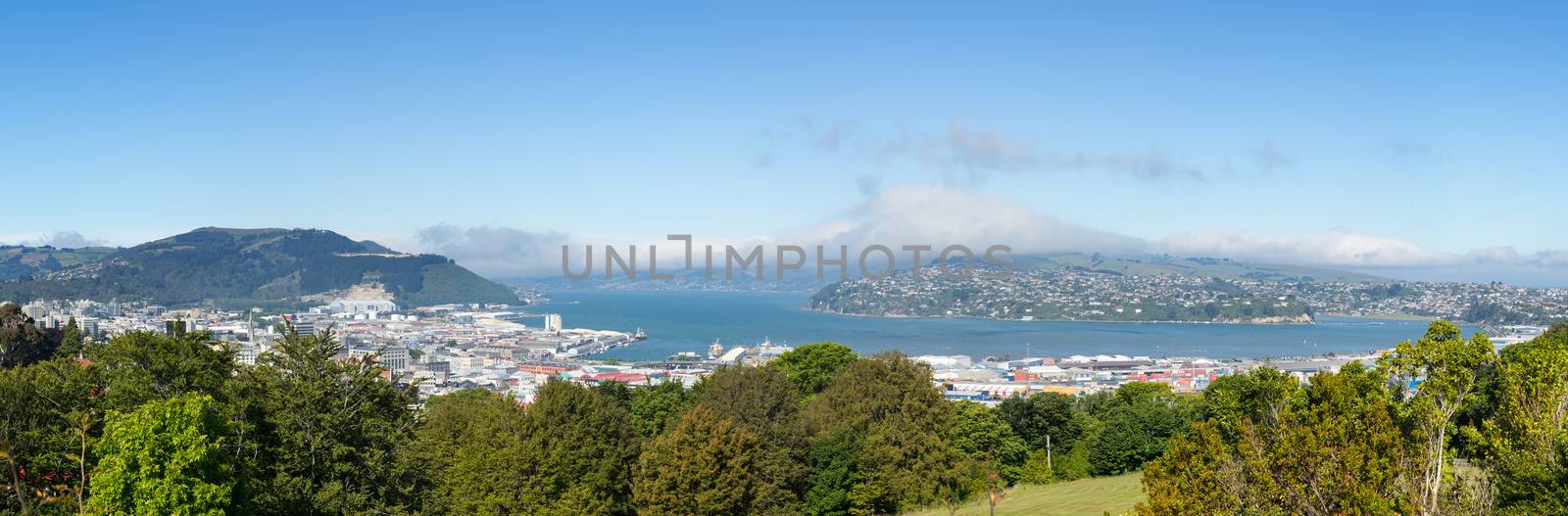 Broad panoramic landscape of the Otago Peninsula and Bay with the city of Dunedin in the foreground and clouds hanging over the mountains