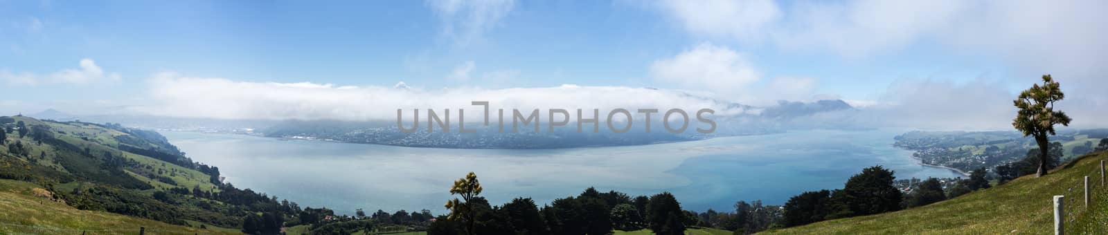 Broad panoramic landscape of the Otago Peninsula and Bay with the city of Dunedin in the distance and clouds hanging over the mountains