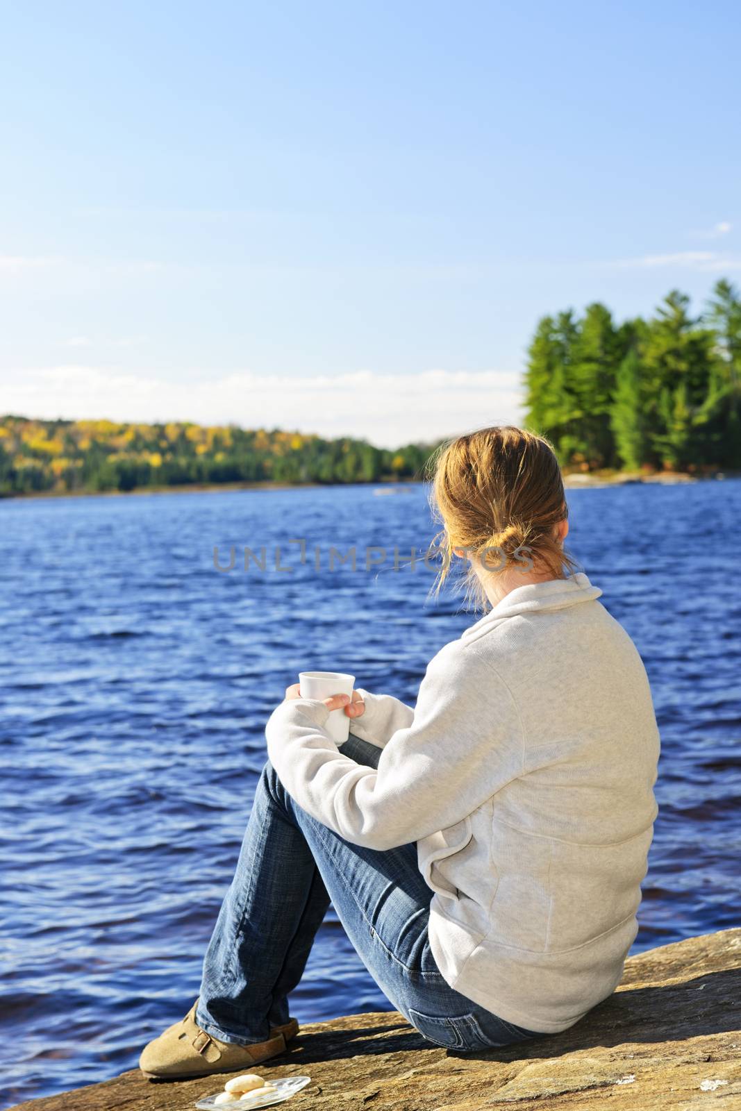 Woman sitting on rock relaxing by beautiful lake in Algonquin Park, Canada.