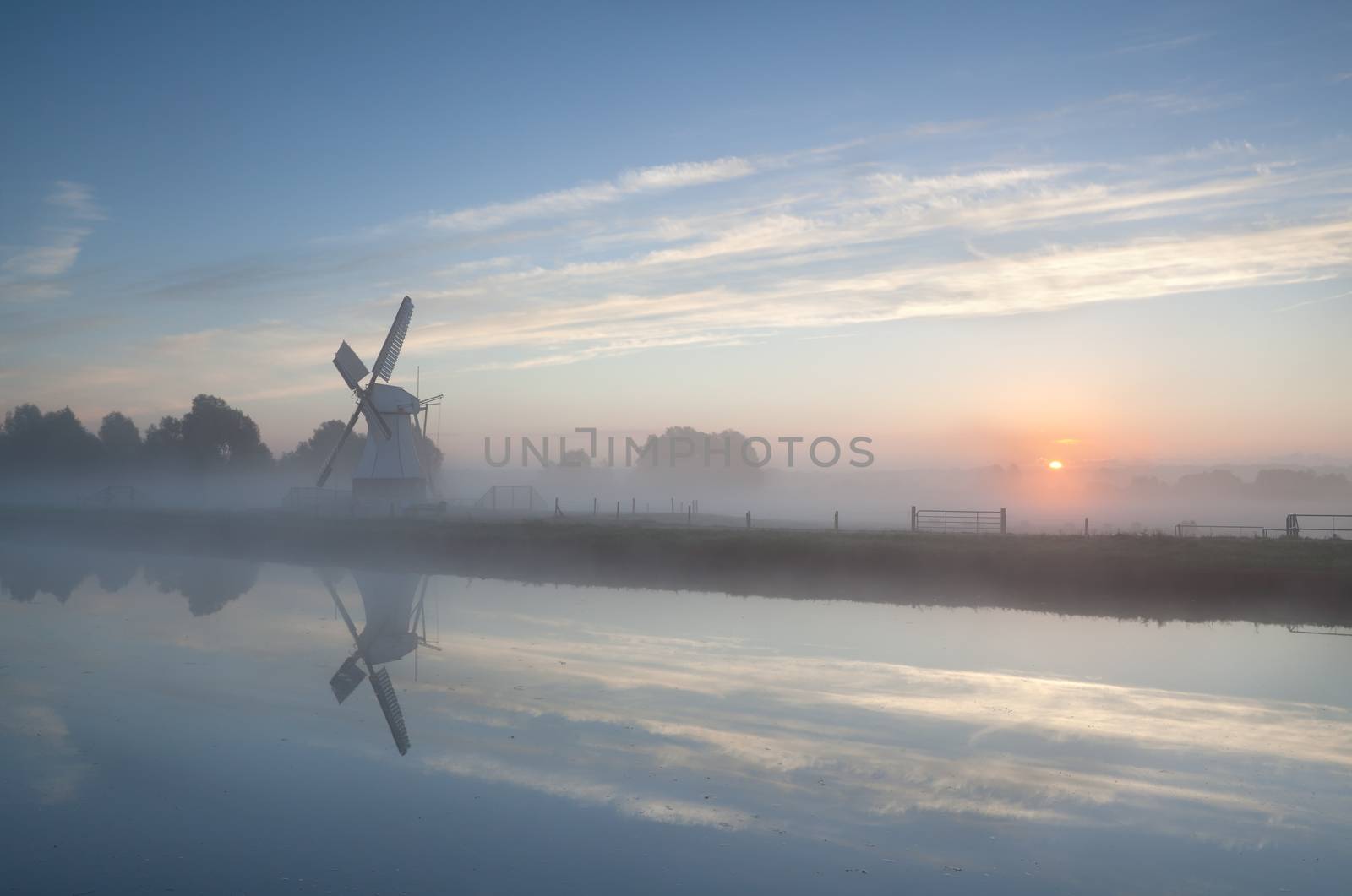 misty sunrise over river and windmill by catolla