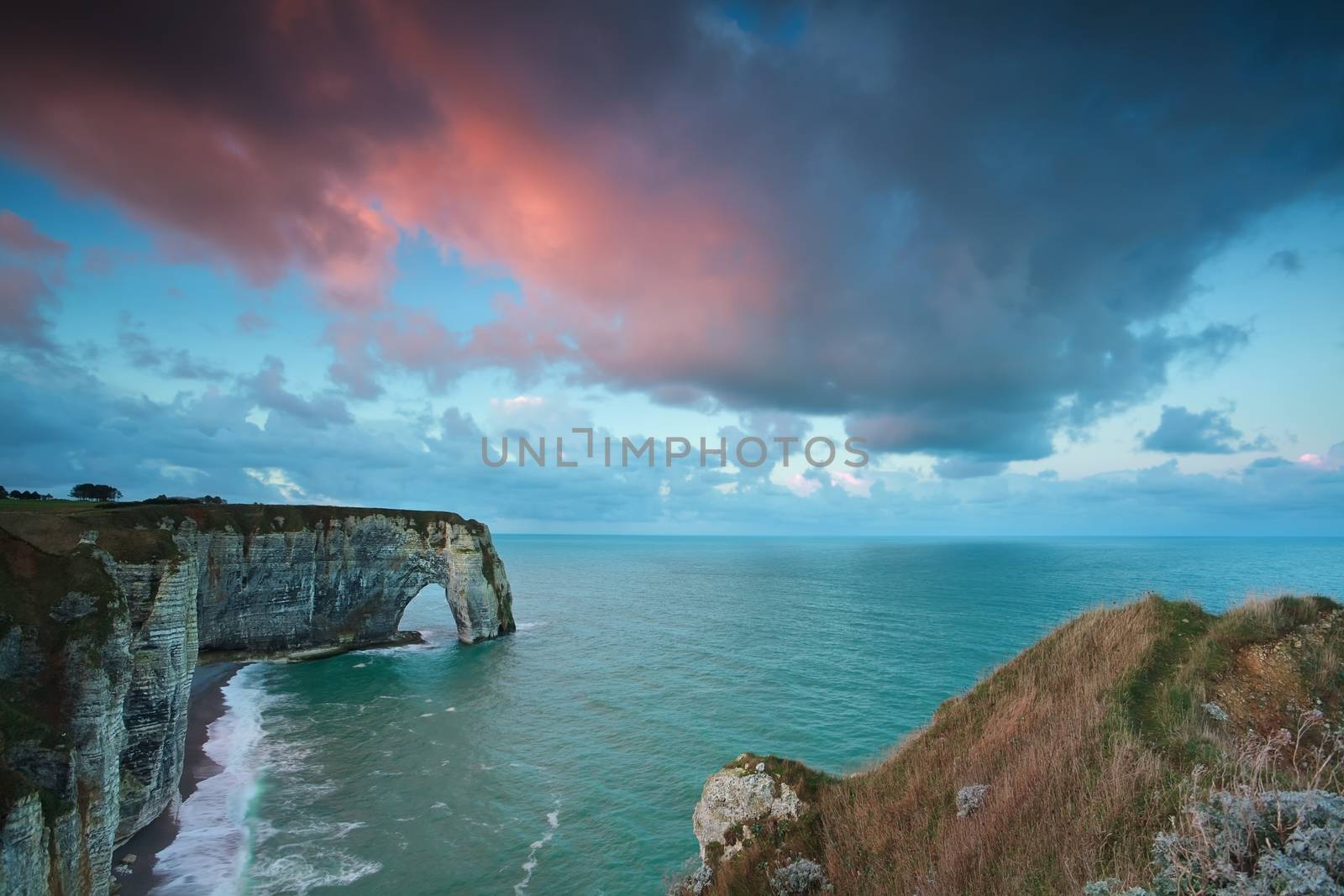 pink stormy sunrise over cliffs in ocean by catolla