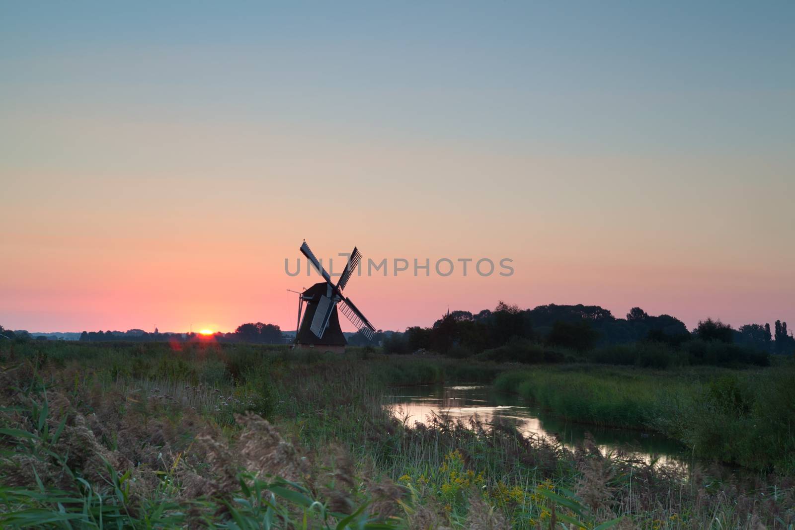 Dutch windmill at sunrise by river, Holland