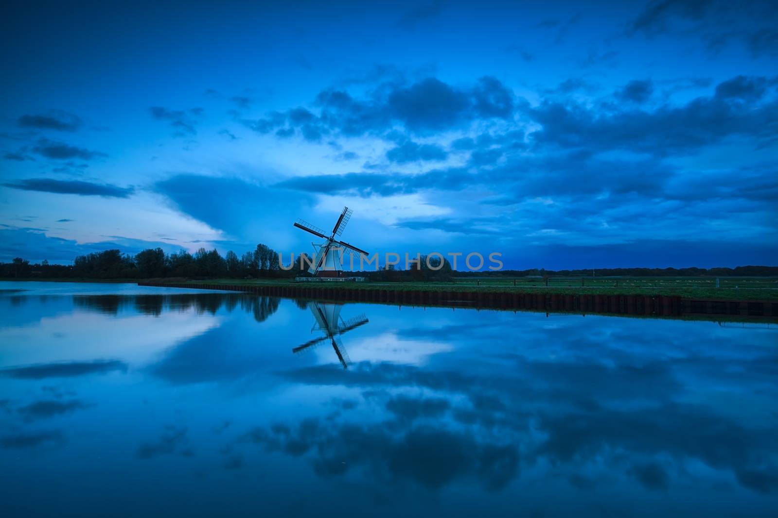 Dutch windmill and clouds in dusk reflected in river, Holland