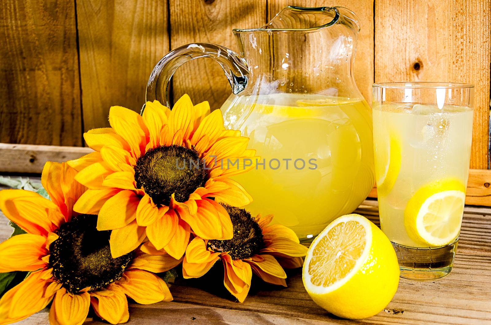 Summer lemonade with lemon slices, pitcher, and sunflowers on wood bench.  