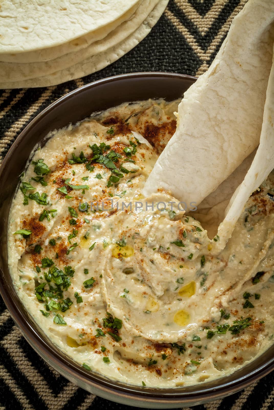 A closeup image of a bowl with a delicious and creamy hummus dip with flat bread.