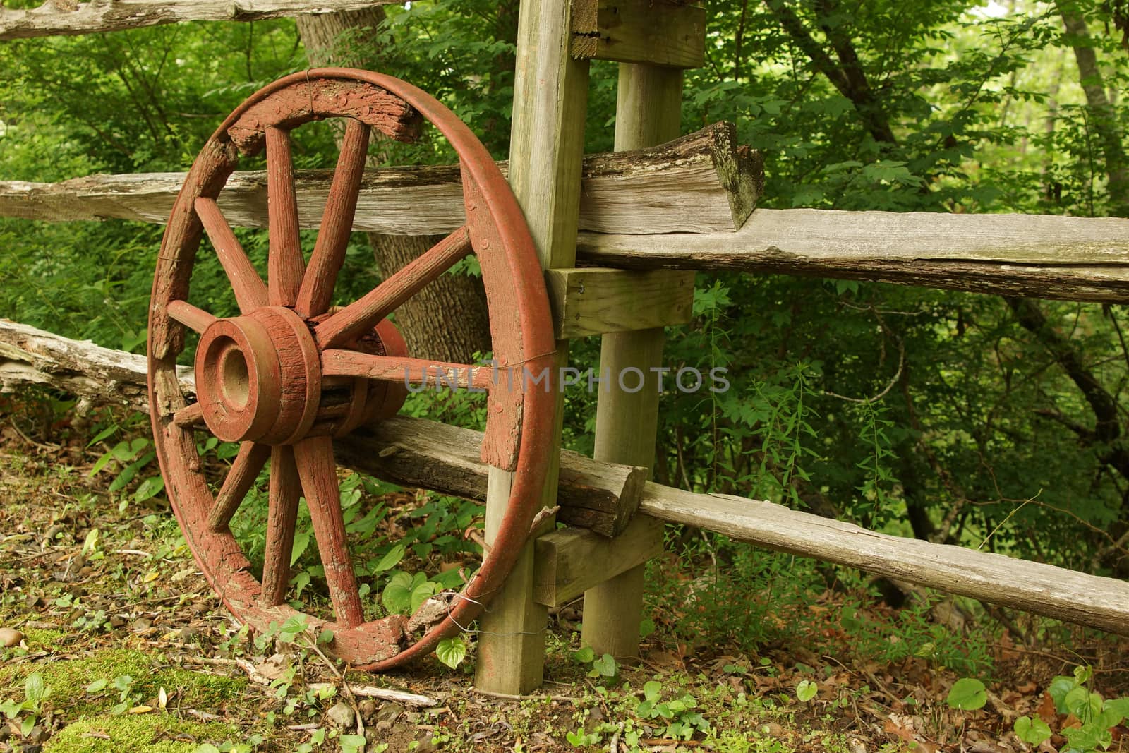 A rustic old wooden wheel against a fence