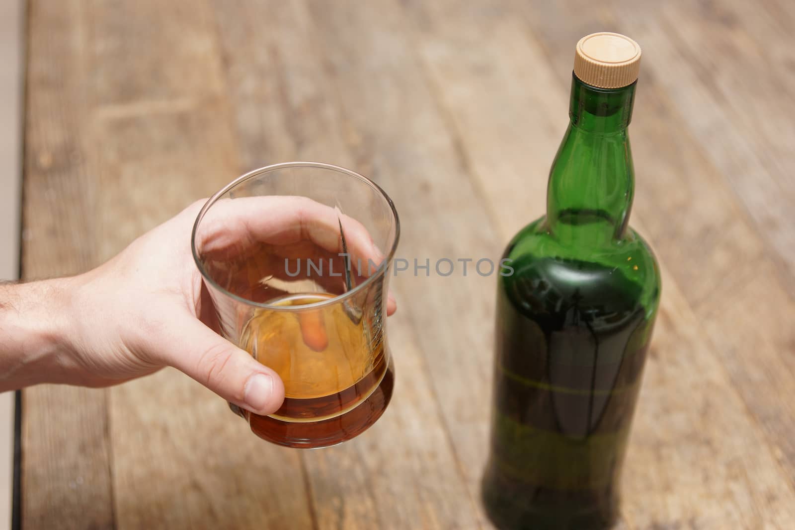 A man holding a glass of scotch next to a bottle