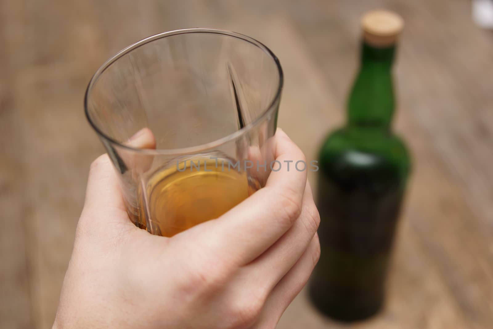 A man holding a glass of scotch next to a bottle