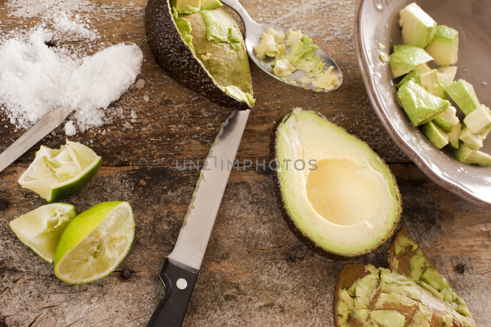 Preparing a delicious fresh avocado salad with a halved avocado next to a bowl with peeled and diced pulp together with a knife, salt and squeezed lemon on an old wooden table, view from above