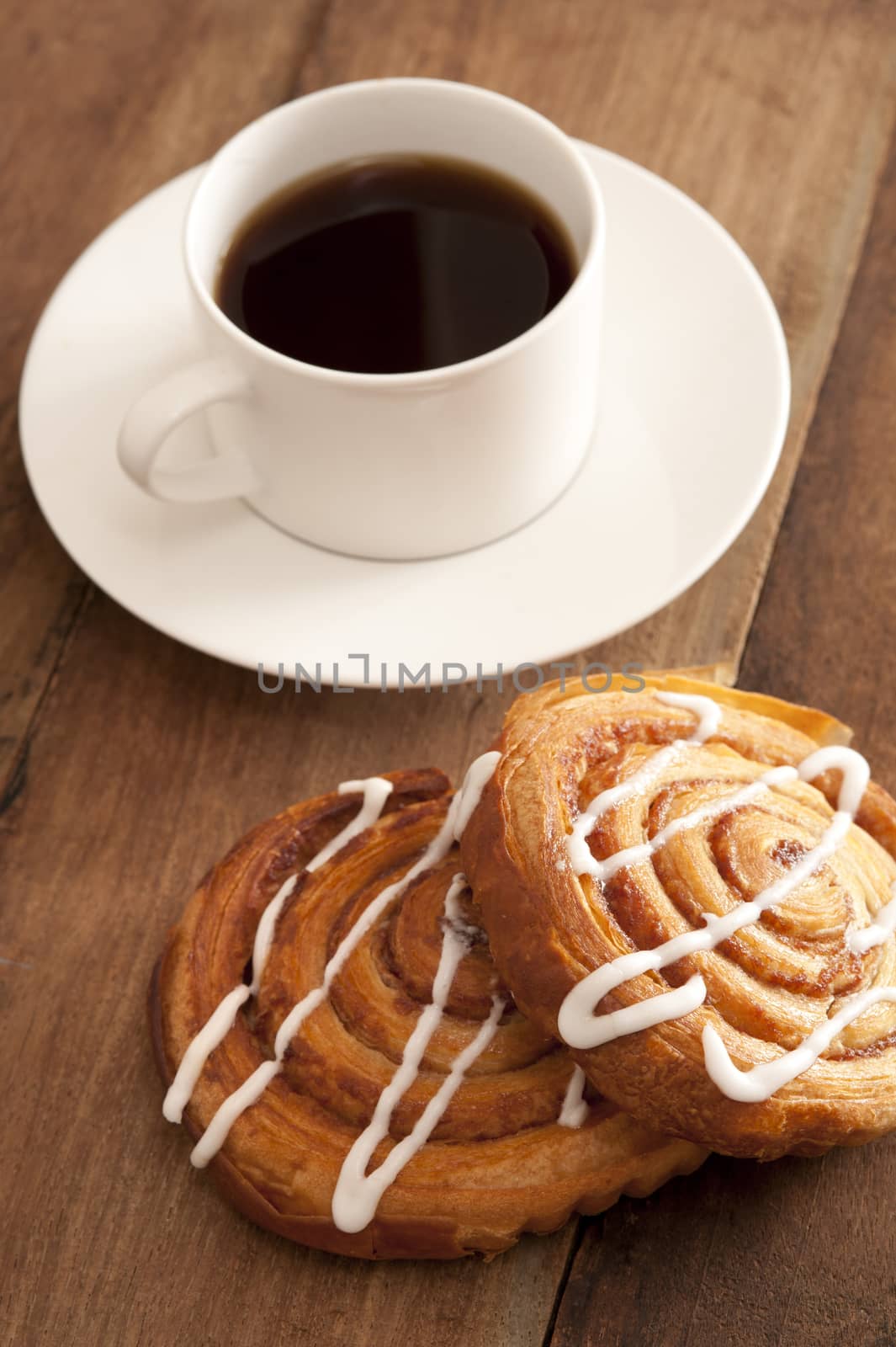 Cup of hot espresso coffee with fresh spiral buns decorated with vanilla icing served on a wooden counter top
