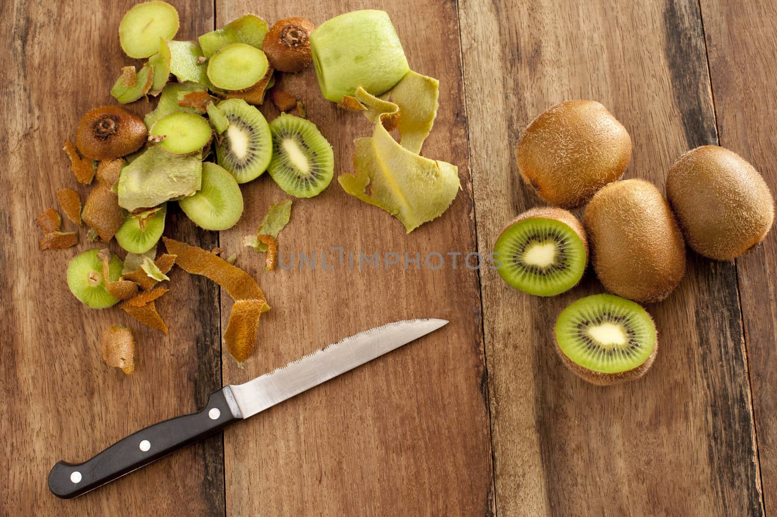 Overhead view of a wooden kitchen counter with a knife and fresh kiwi fruit that are being peeled and diced for a healthy delicious tropical dessert