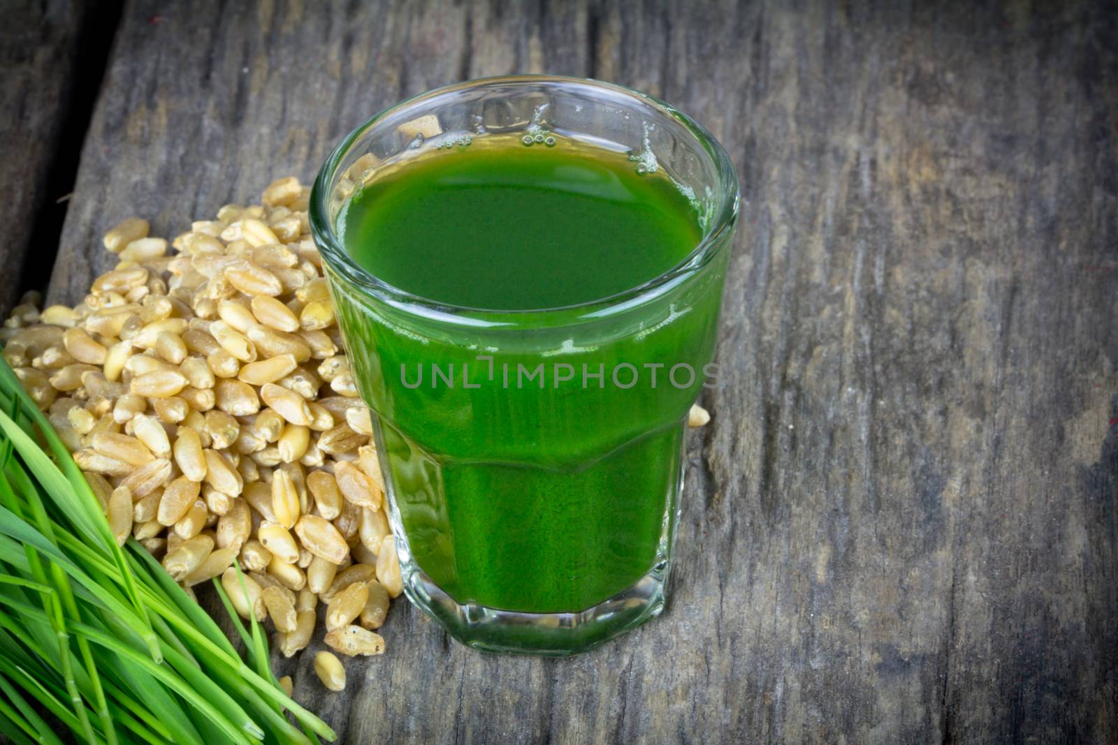 Wheat grass juice with fresh wheat grass and wheat on wood background