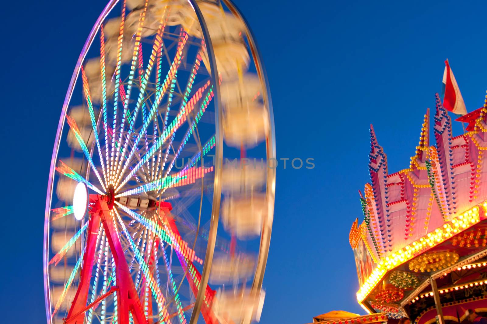 The circular motion of a carnival ferris wheel blurs against a cobalt blue twilight sky at a county fair. 