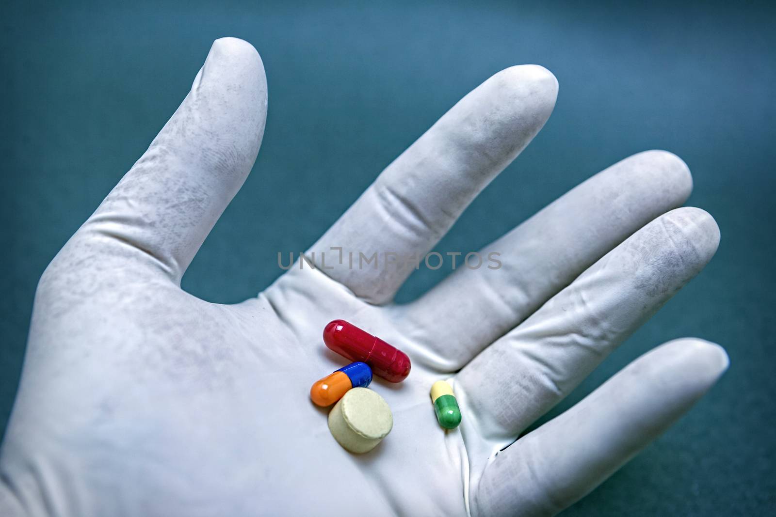 Hand with white latex glove turning various pills