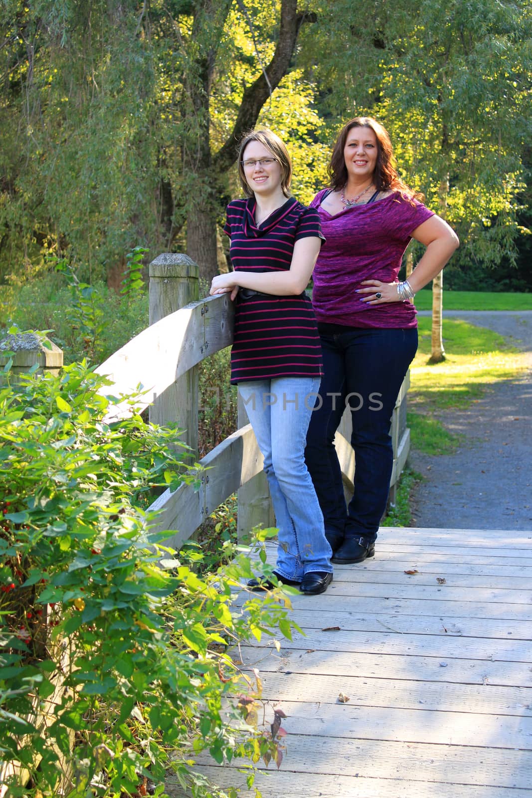 Attractive mother and daughter family standing on a wooden bridge in the outdoors