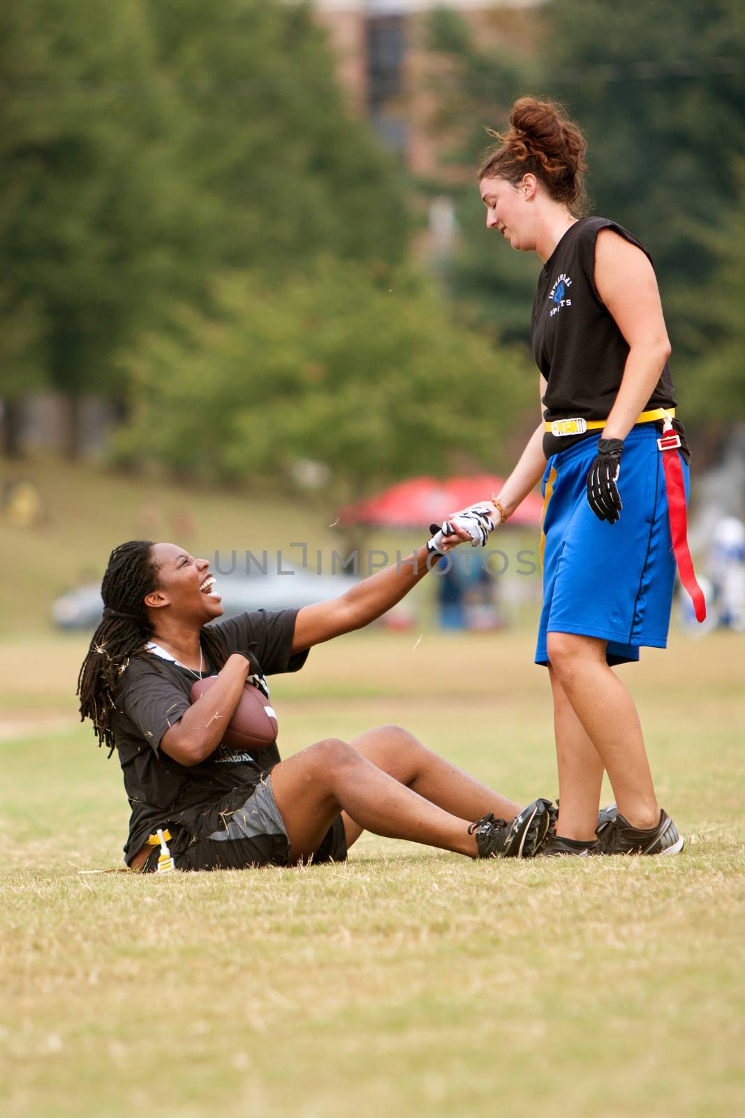 Atlanta, GA, USA - September 29, 2012:  One player lends a hand to help a teammate off the ground, during practice for the Krush team of the Atlanta Women's Flag Football League.  The practice was held at an Atlanta public park.