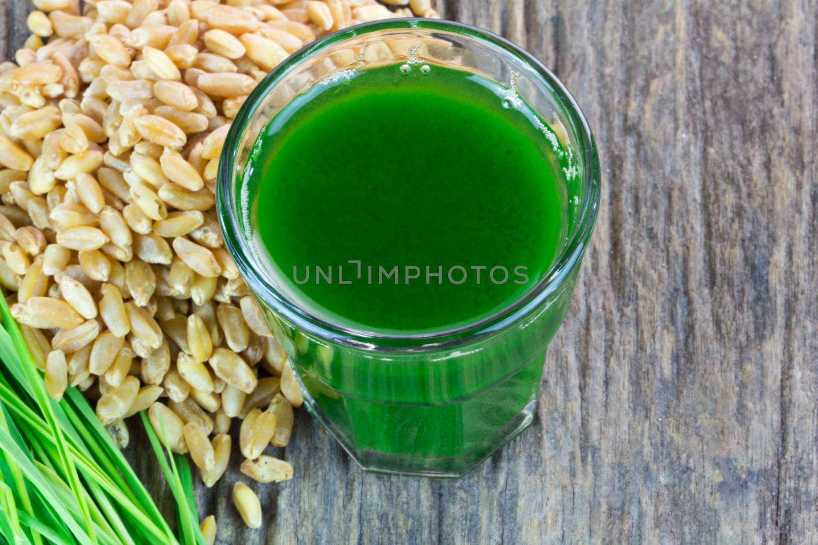 Wheat grass juice with seed and wheat on wood background 