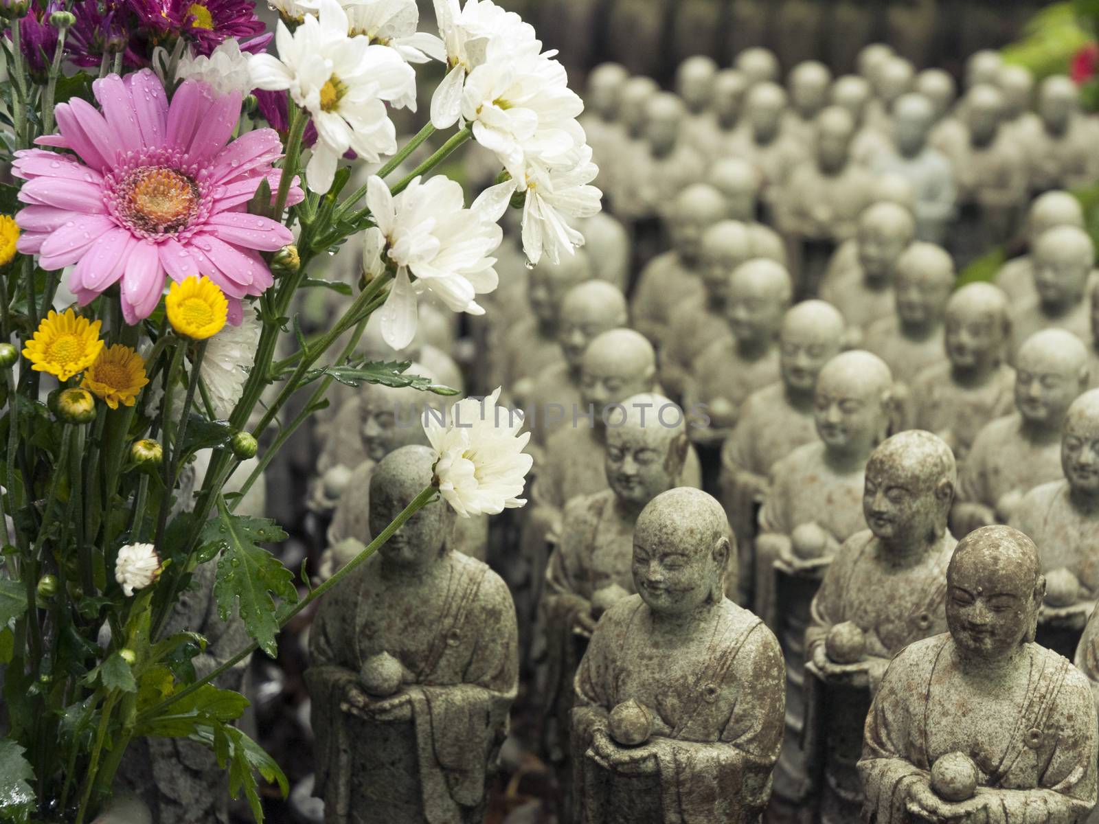 rows of similar japanese jizo sculptures in Hase-Dera temple, Kamakura, Japan with focus on flowers

