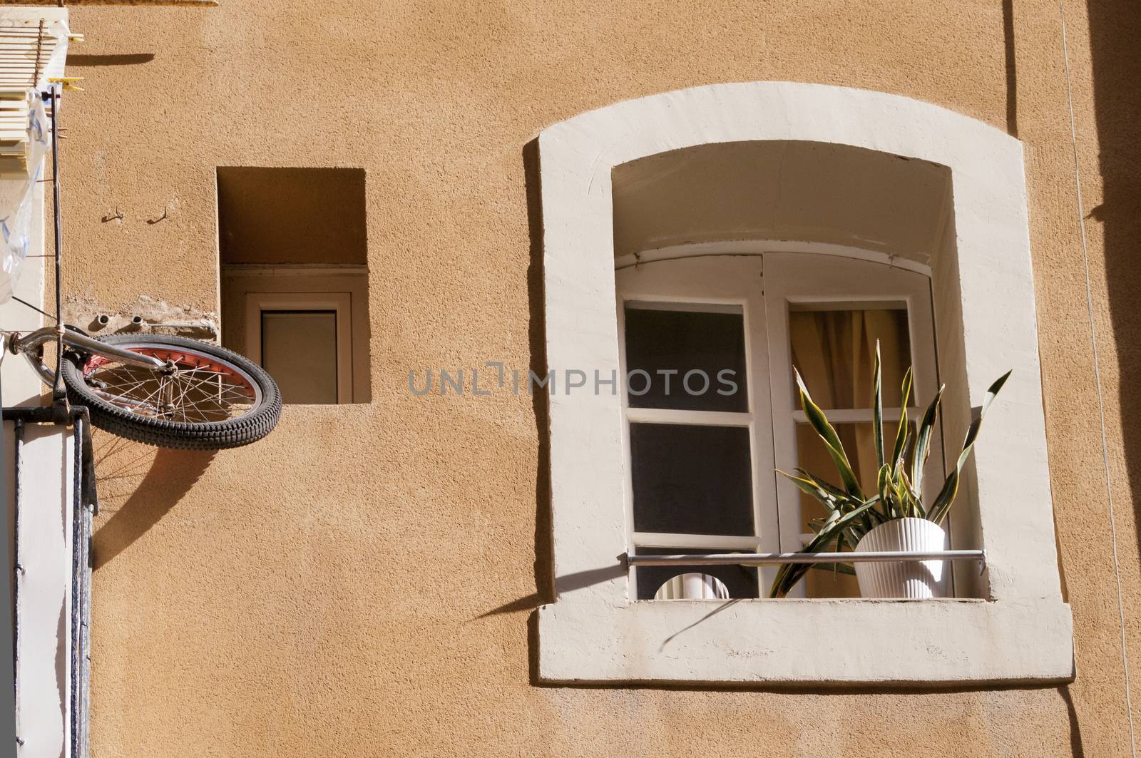 bicycle wheel hanged on balcony and arch window with flowerpot at old building facade